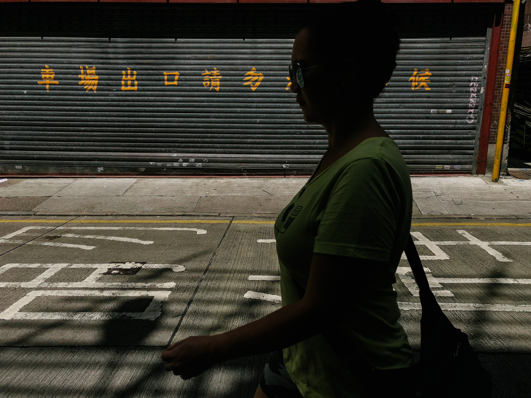 A woman walks across the photo. In the background, and on the street, Chinese characters are written 