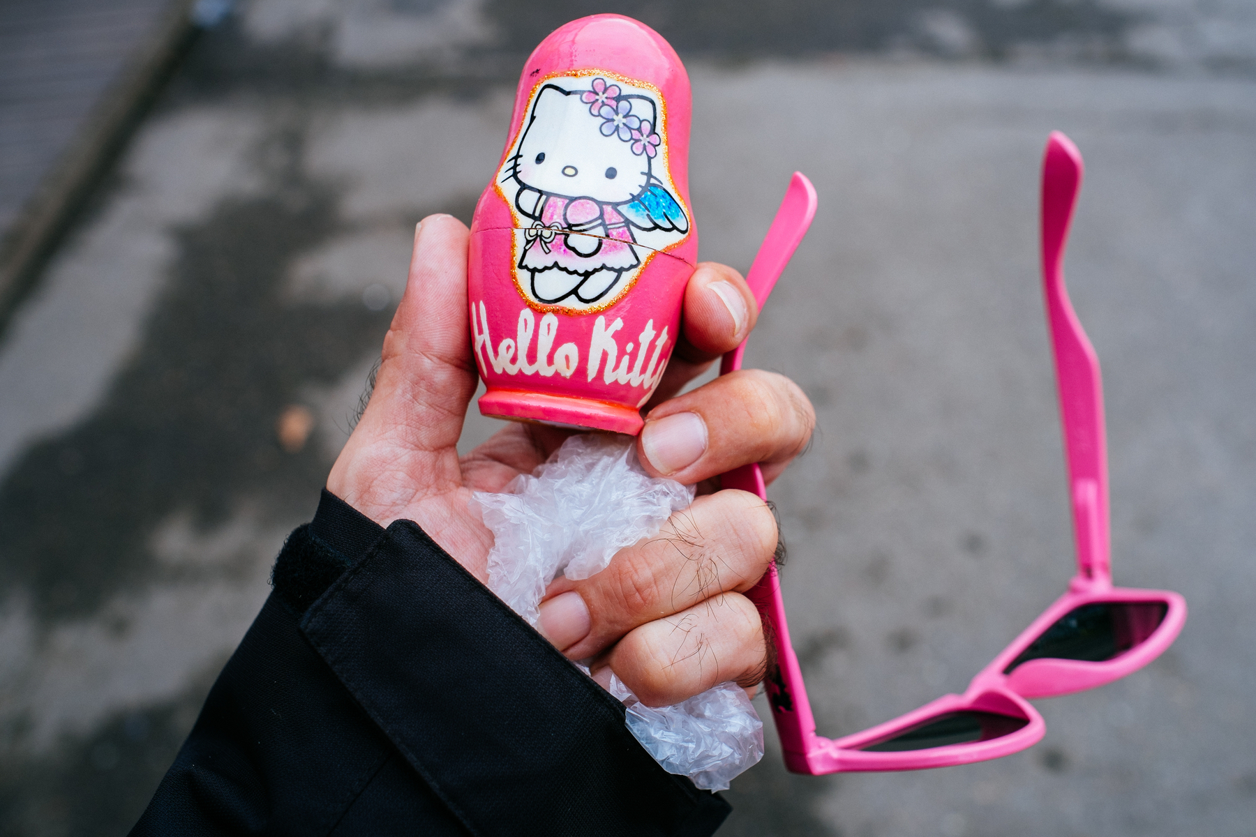 A hand holding a pair of pink shades, and a pink matryoshka doll with Hello Kitty painted on it 