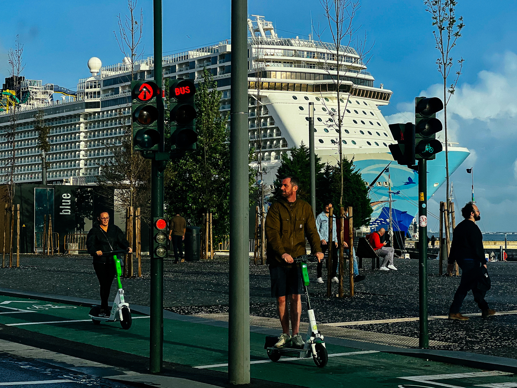 People use scooters and walk by a huge cruise ship
