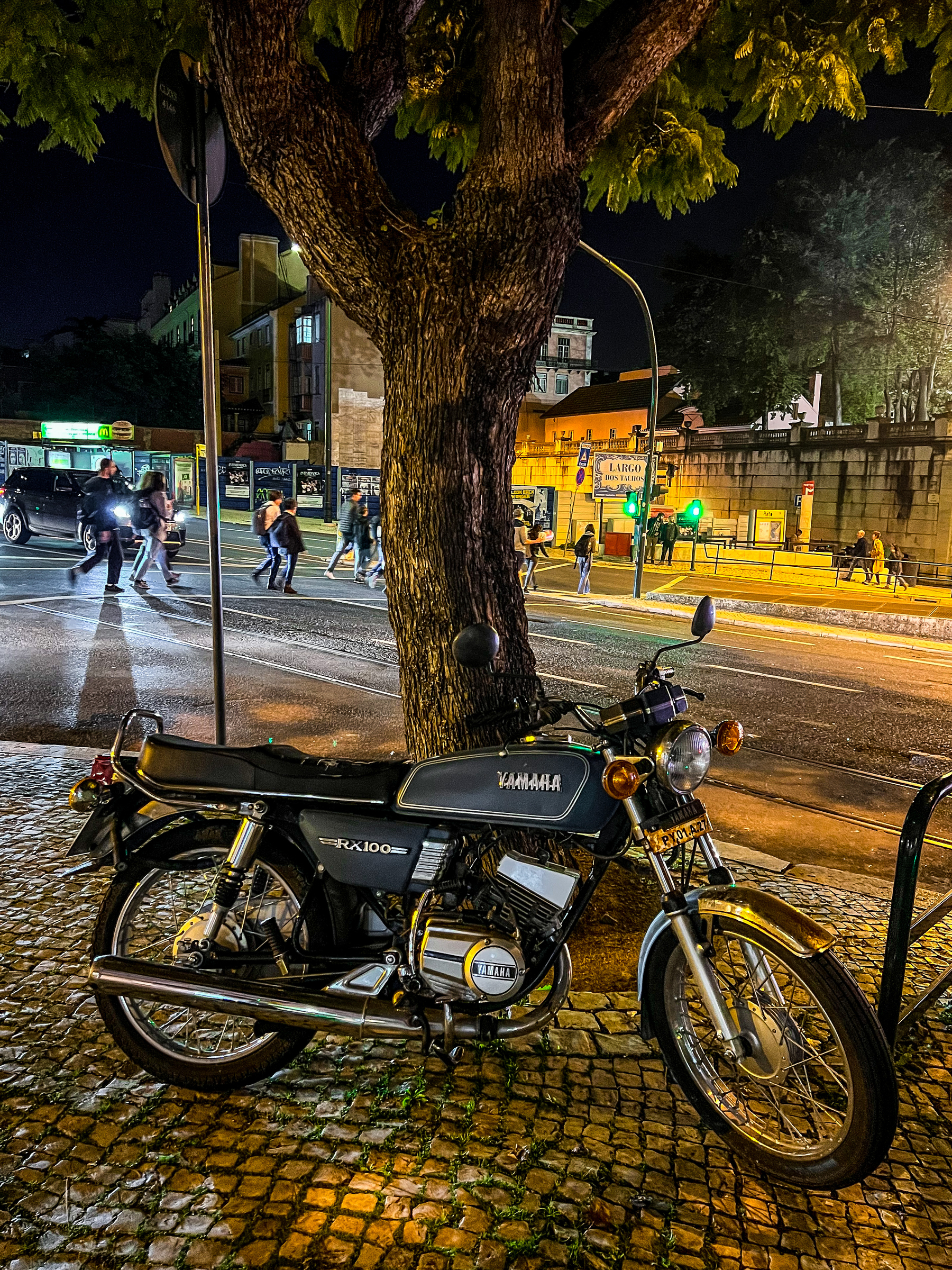night shot, a motorcycle parked under a tree, city life in the back