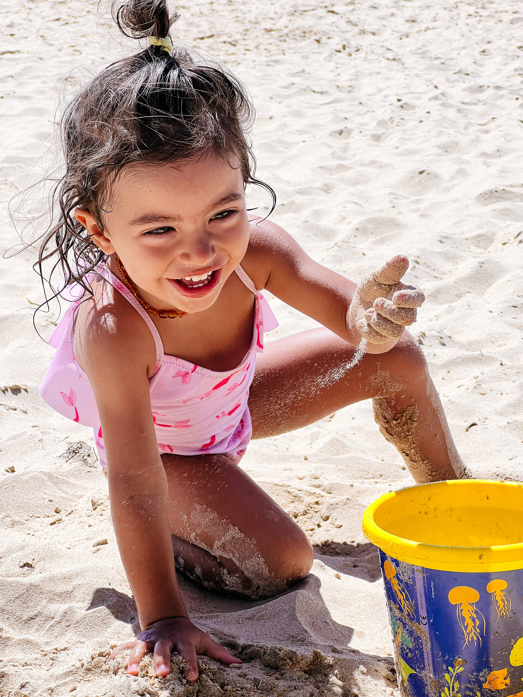 a toddler has fun with sand, at the beach