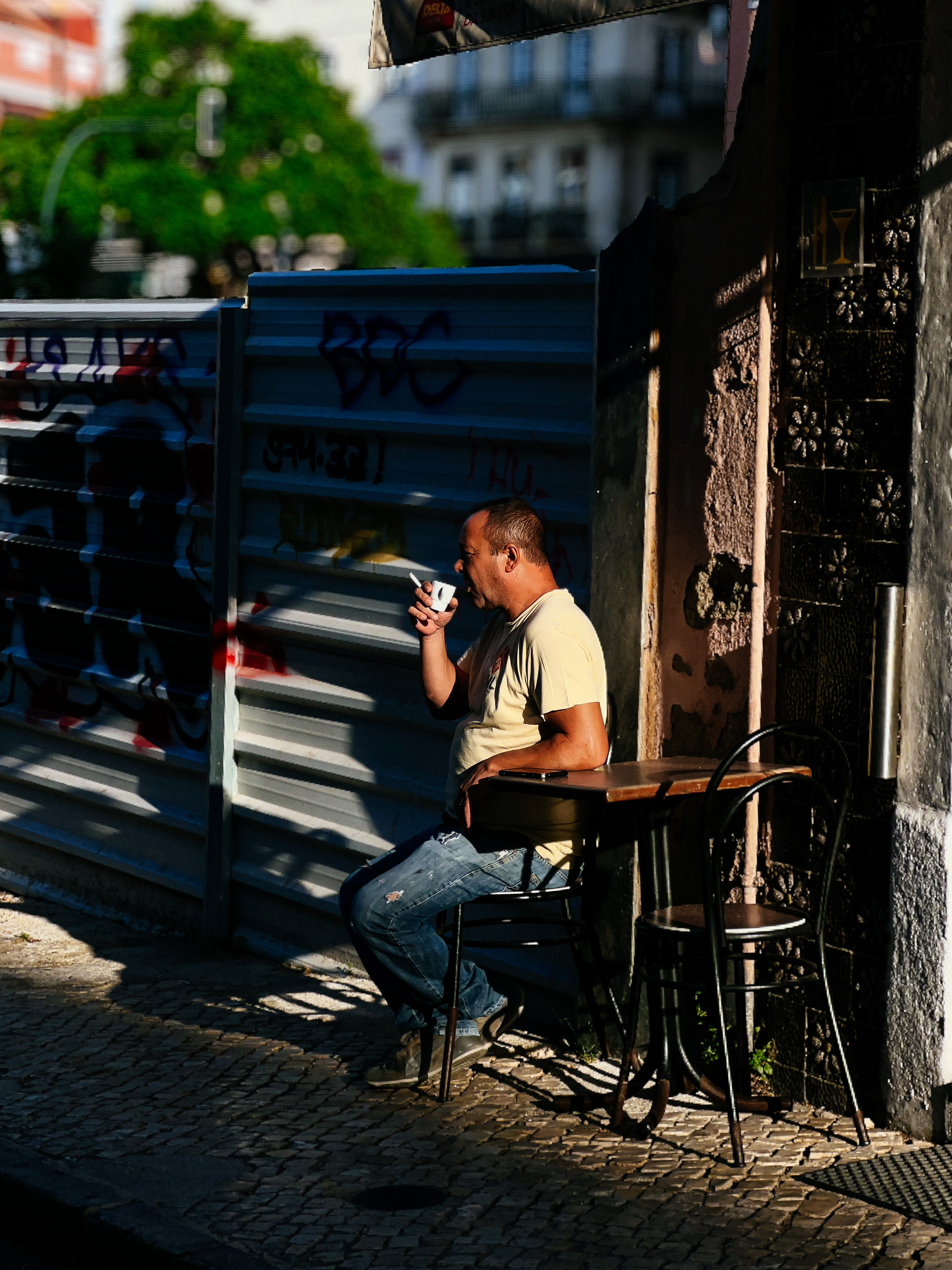 A man sits alone having his morning coffee on a table outside a small cafe, near a construction site.