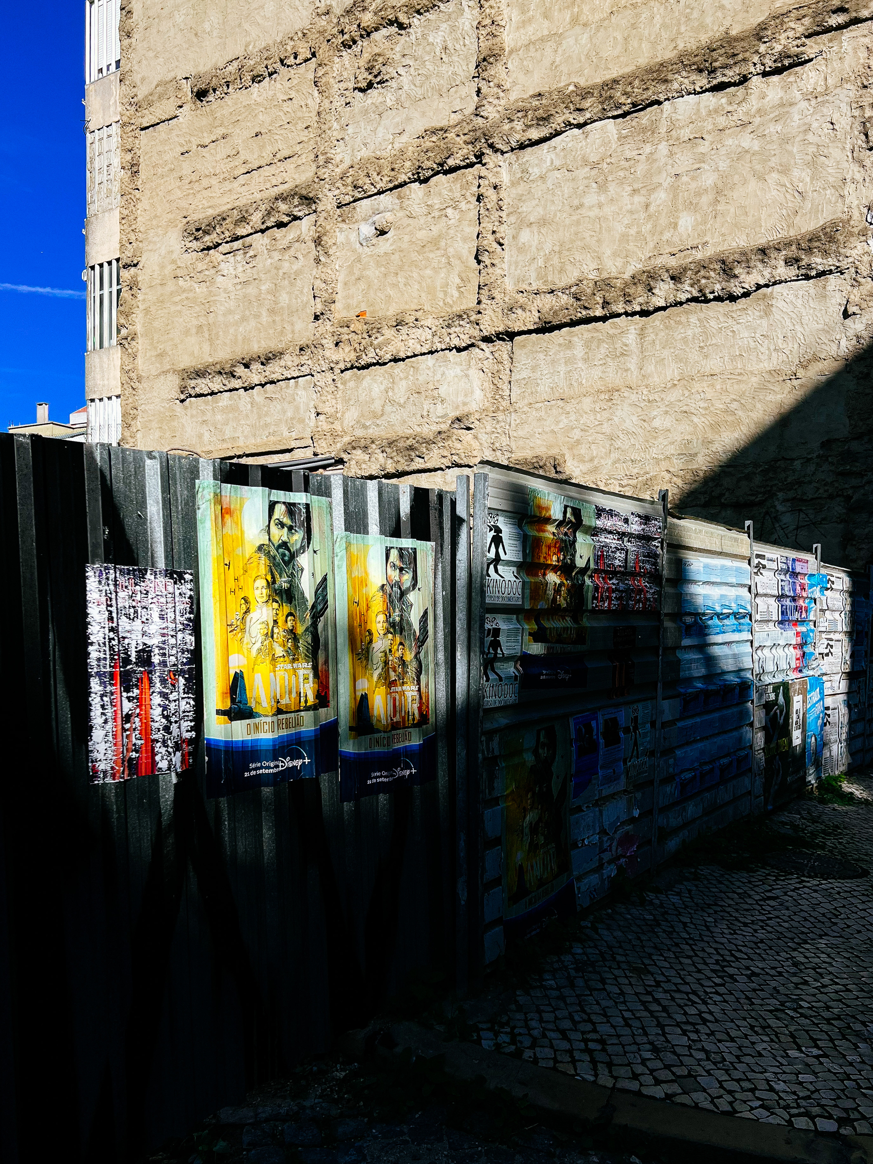 Posters on a fence, in front of a derelict building 