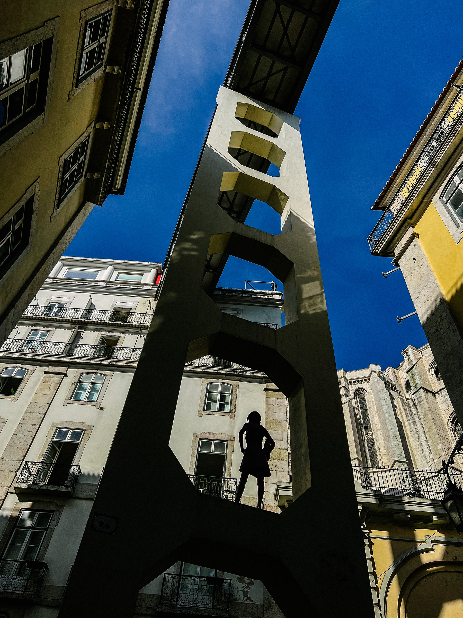 Looking up into an old part of town, a street art mannequin is seen, backlit
