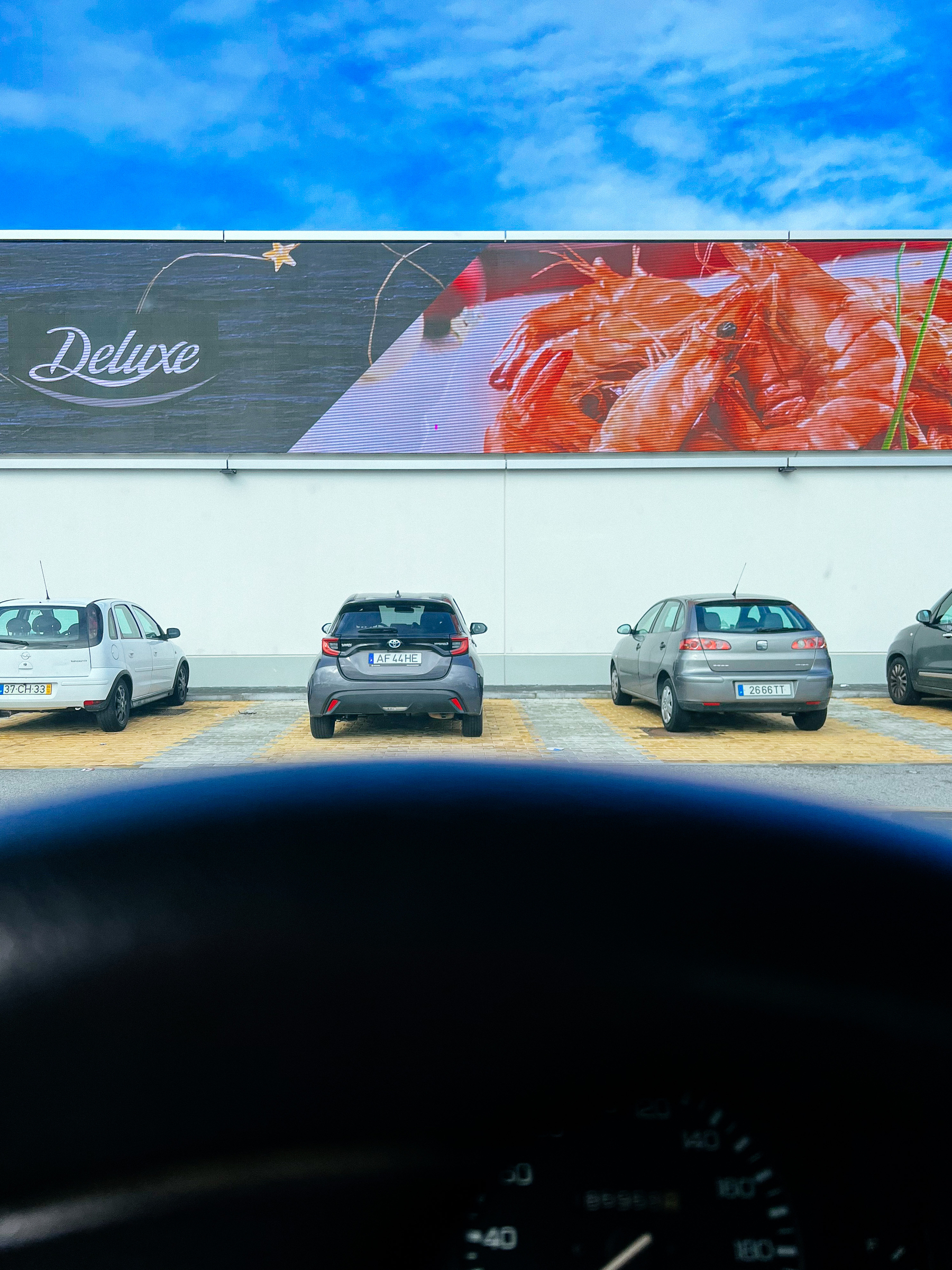 Viewed from inside a car, a parking lot, and a huge ad for shrimp, some cars parked under it. 