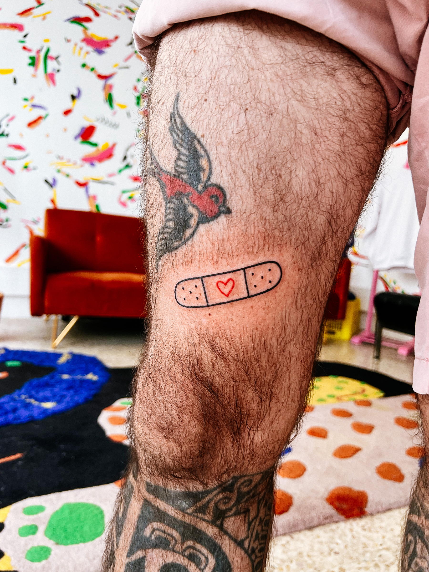 A leg with a couple of tattoos. The new one is a bandaid with a red heart in the middle. 