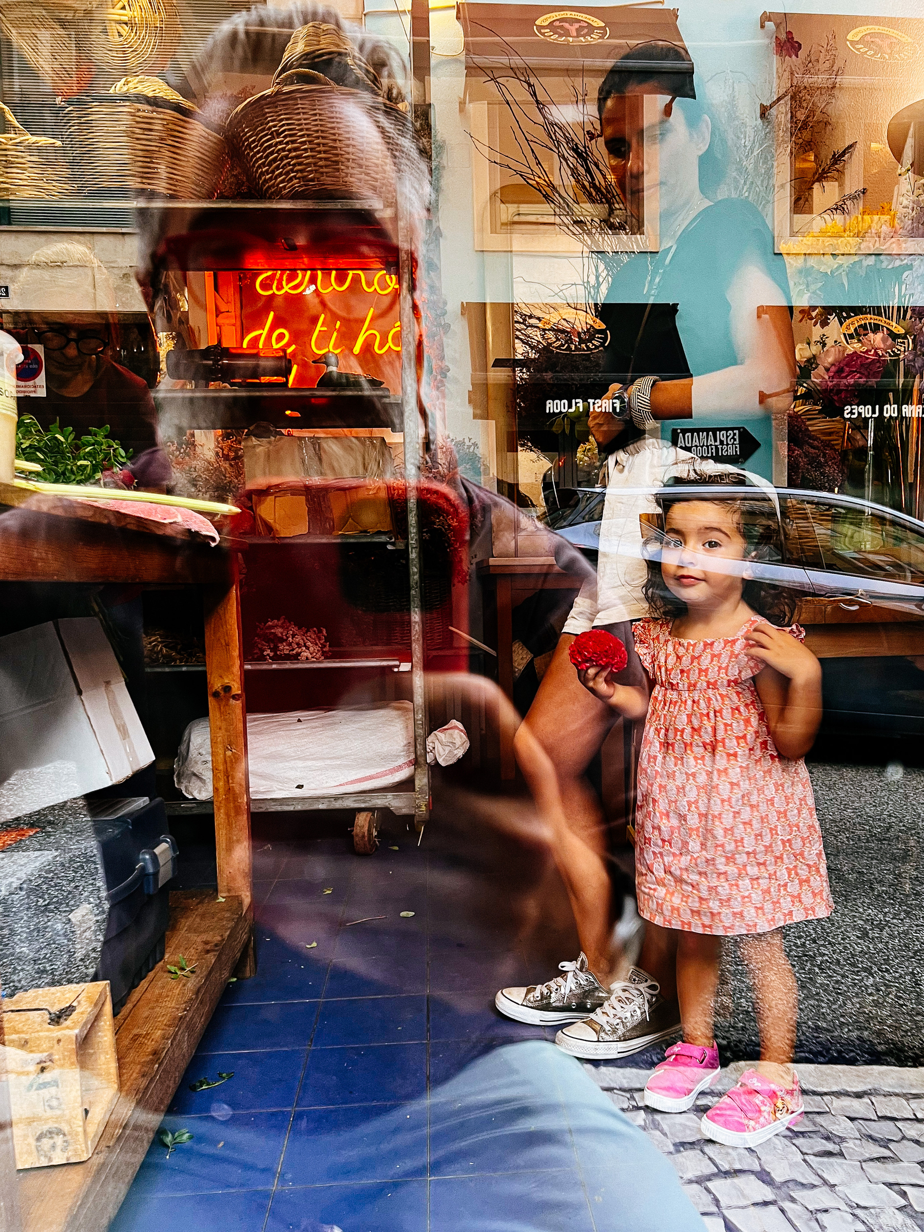 Three people in the photo. Two inside a shop, one reflected on the door window. 