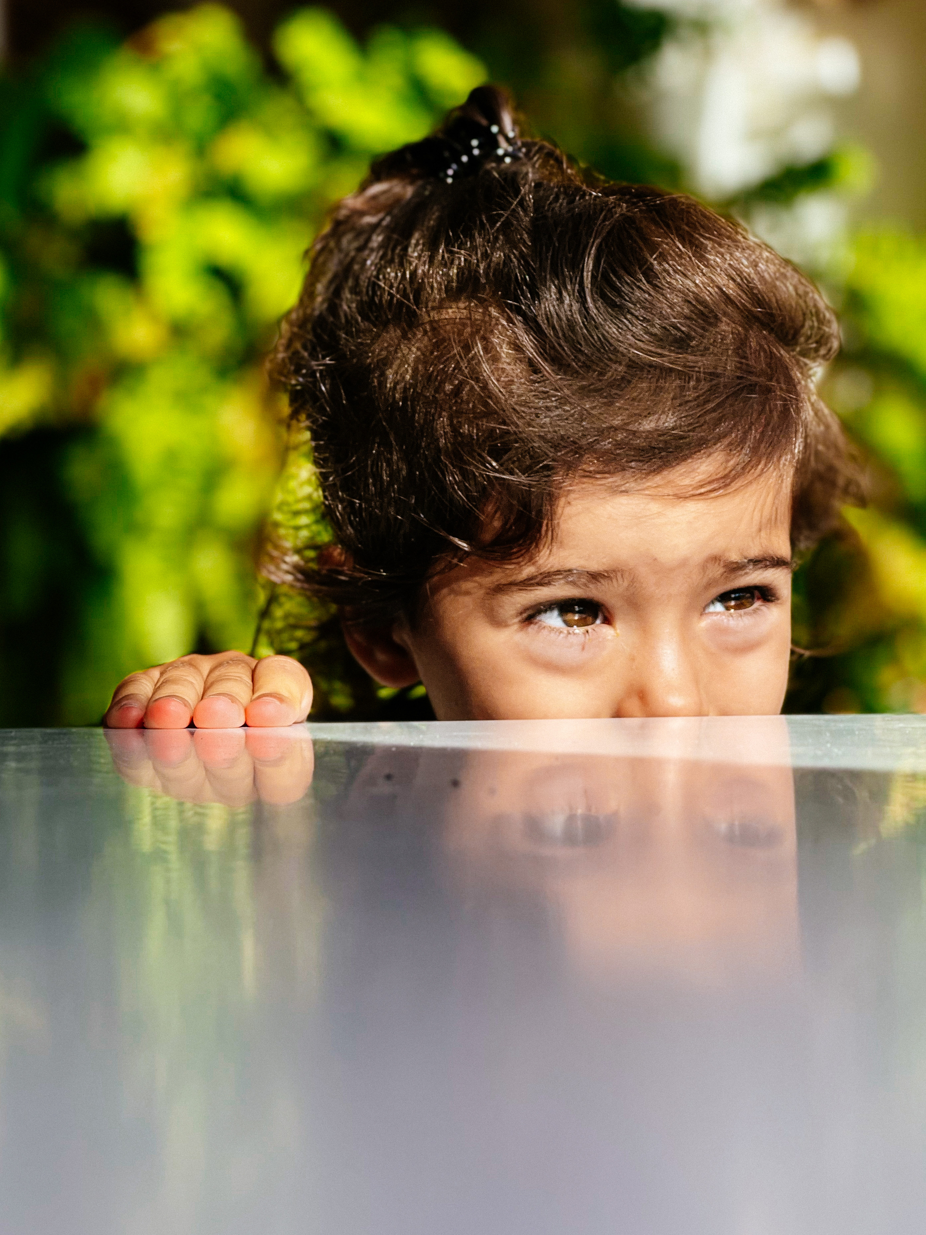 a toddler looks out from behind a table