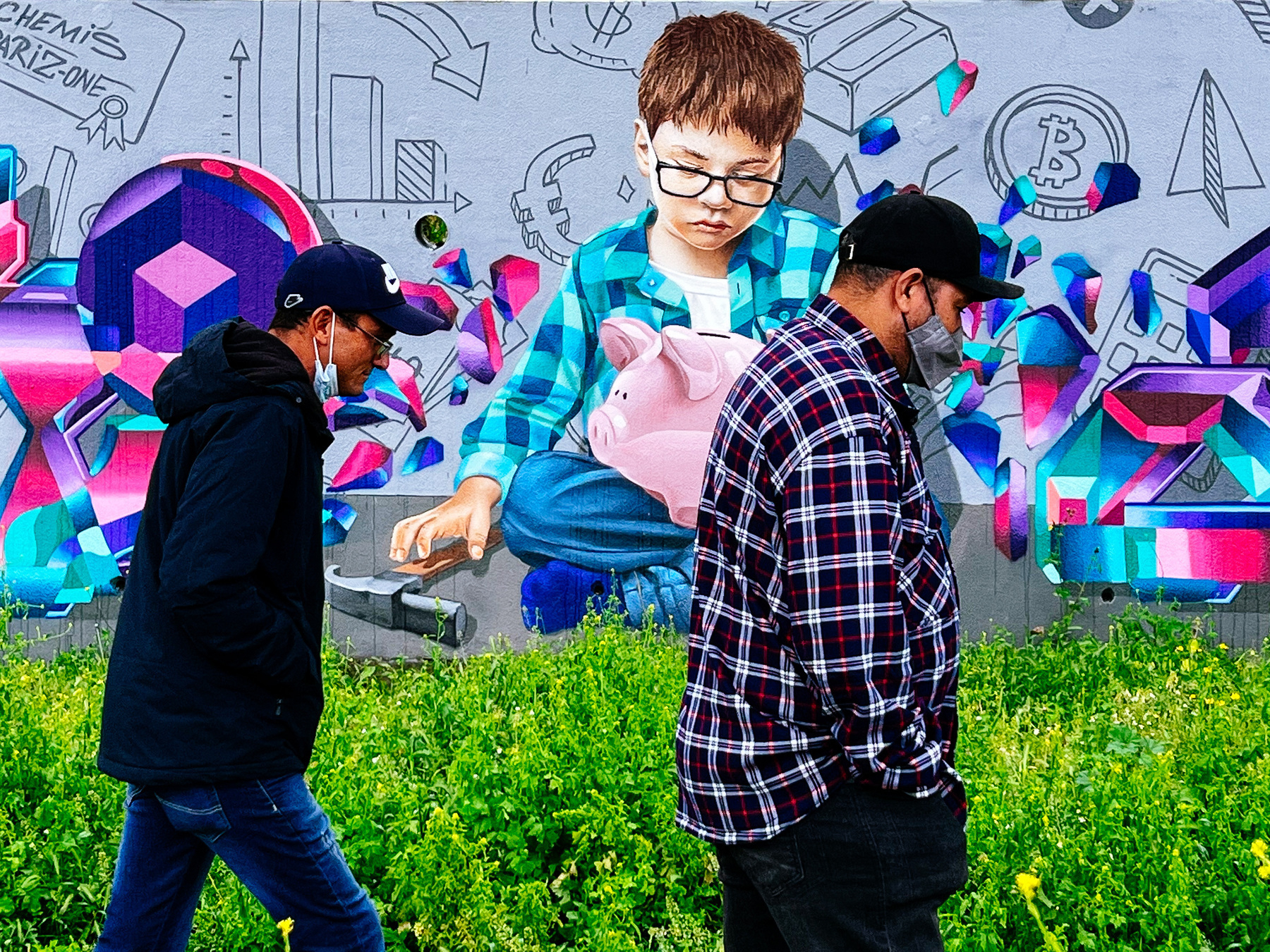 two men walk by a street art piece showing a kid holding a hammer, looking at a piggy bank. next to him are several signs, including one for bitcoin.