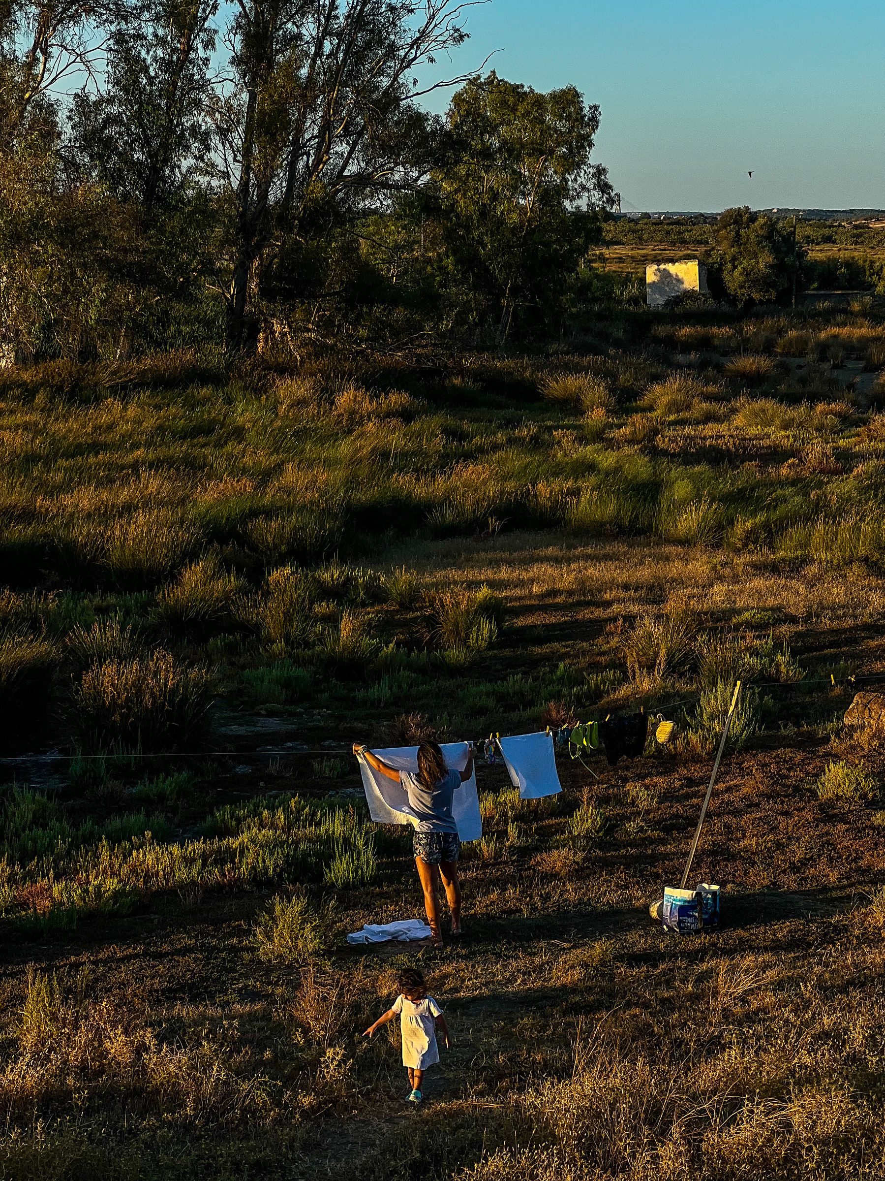 a woman hangs laundry to dry in the field, with a toddler close by