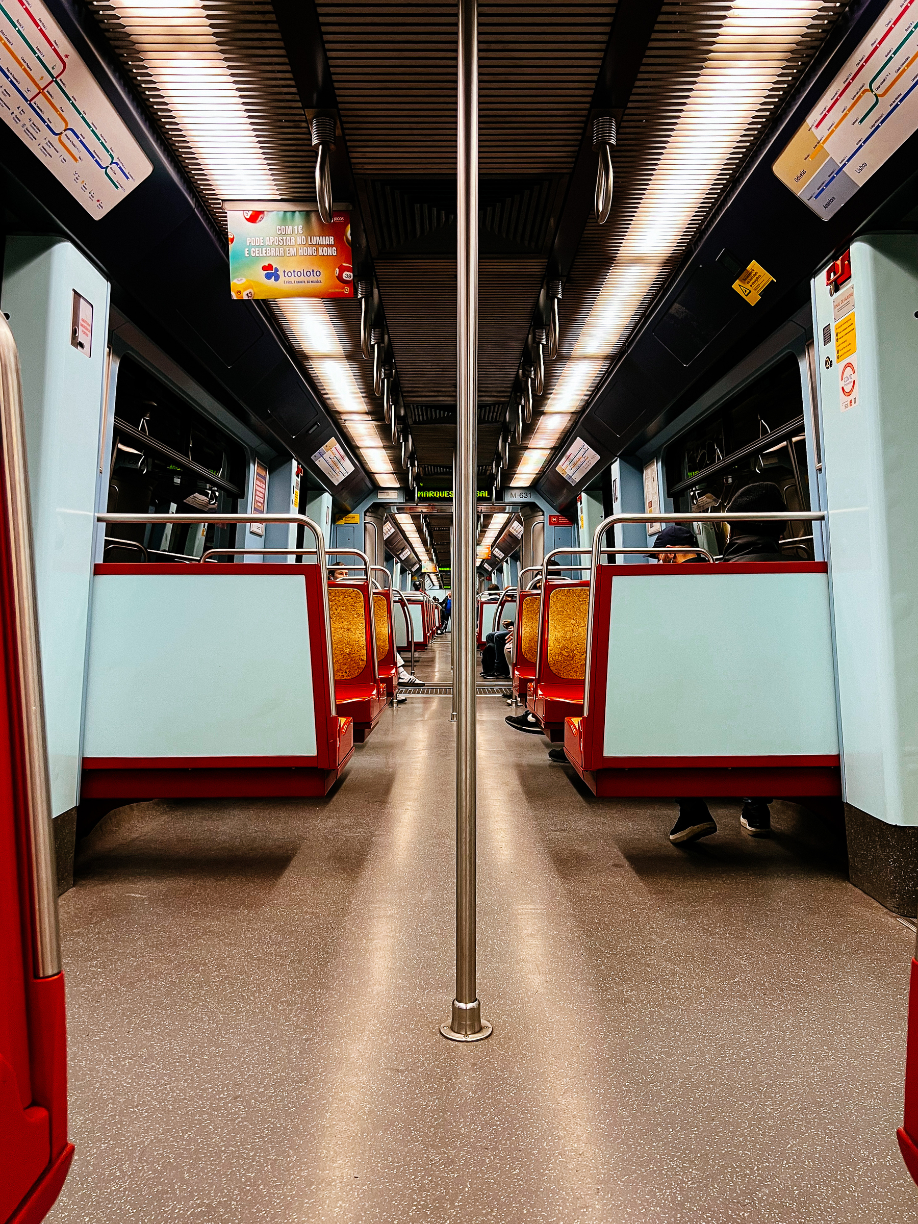 Inside a subway car, the seats pale blue and red. Mostly empty. 