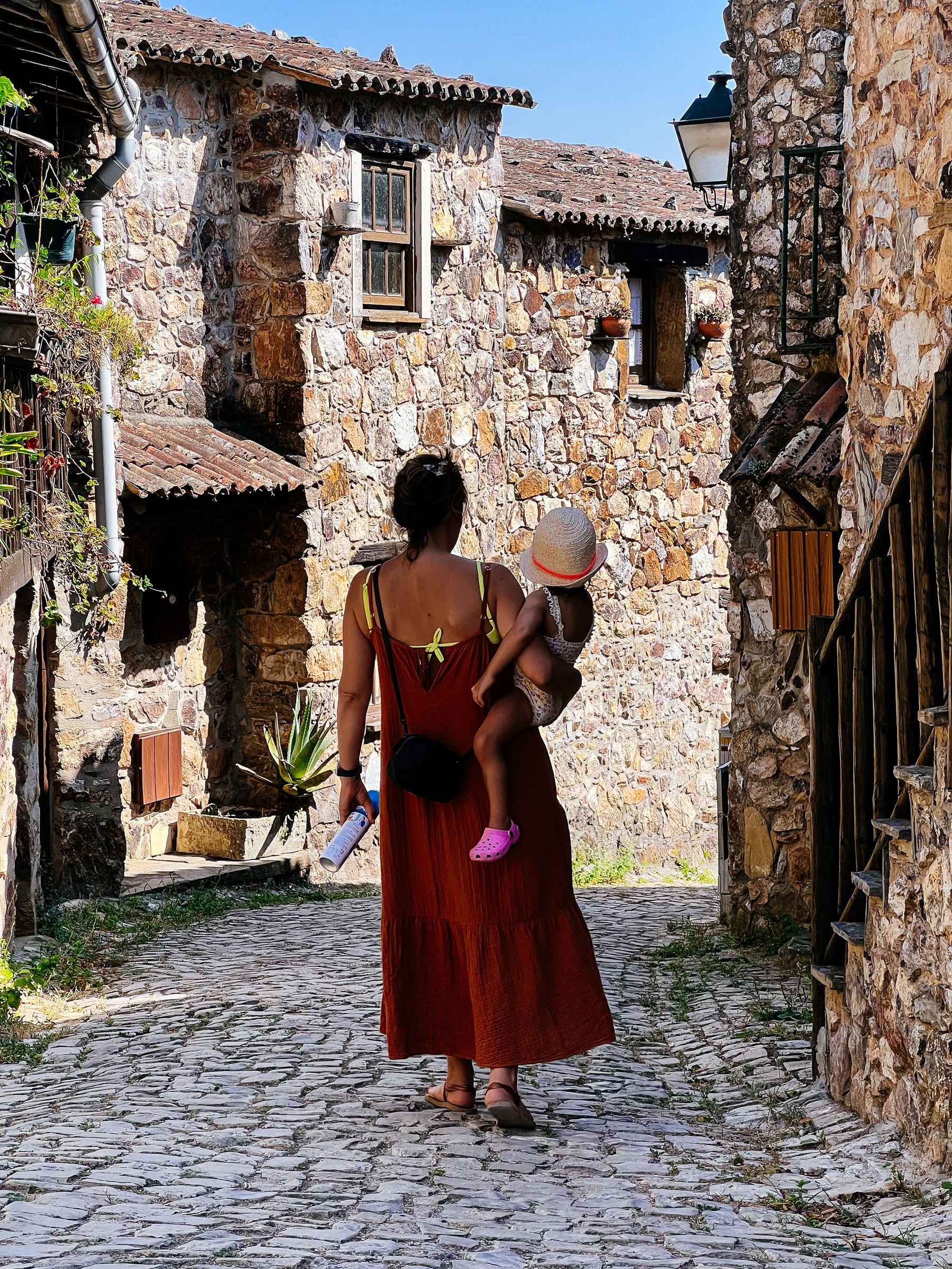 A mom and daughter walk down a rustic looking street. 