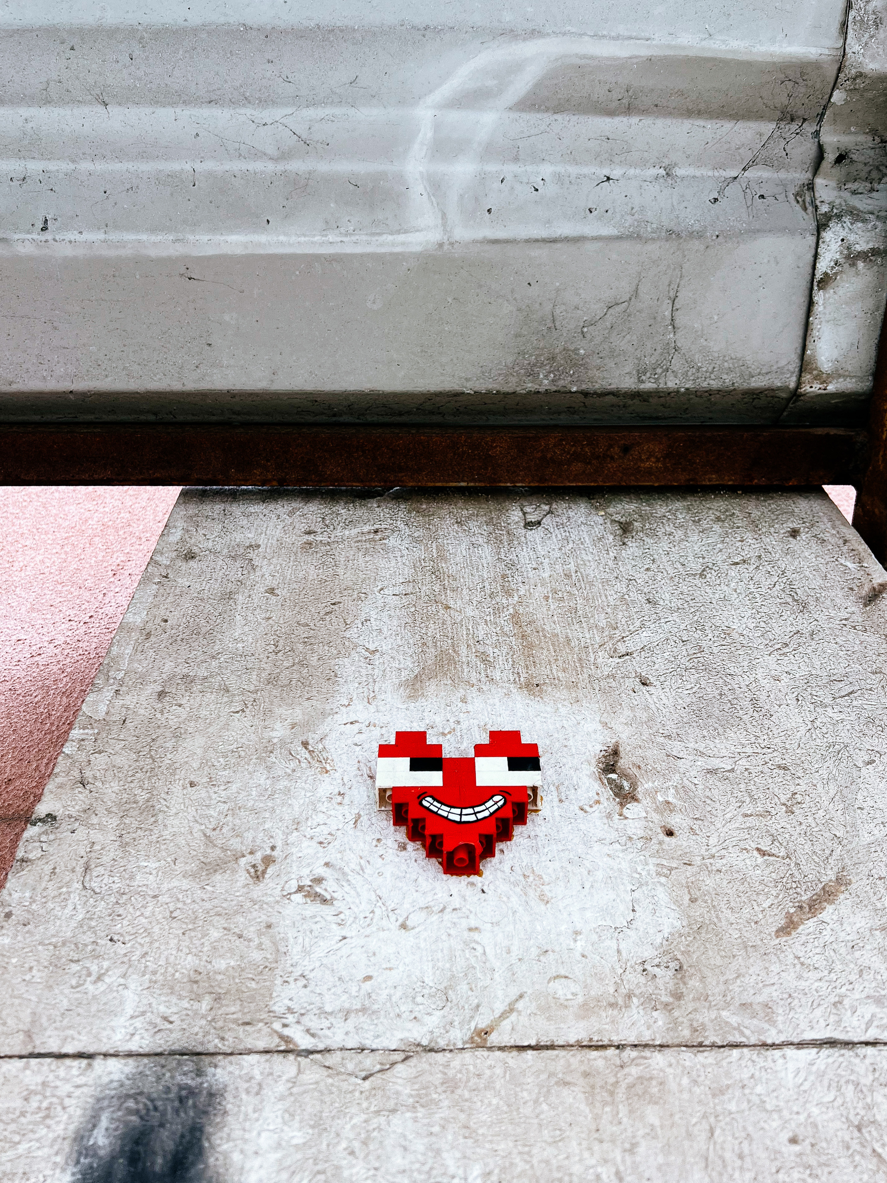 A heart with eyes and a face, made of LEGO pieces, glued to a wall. 