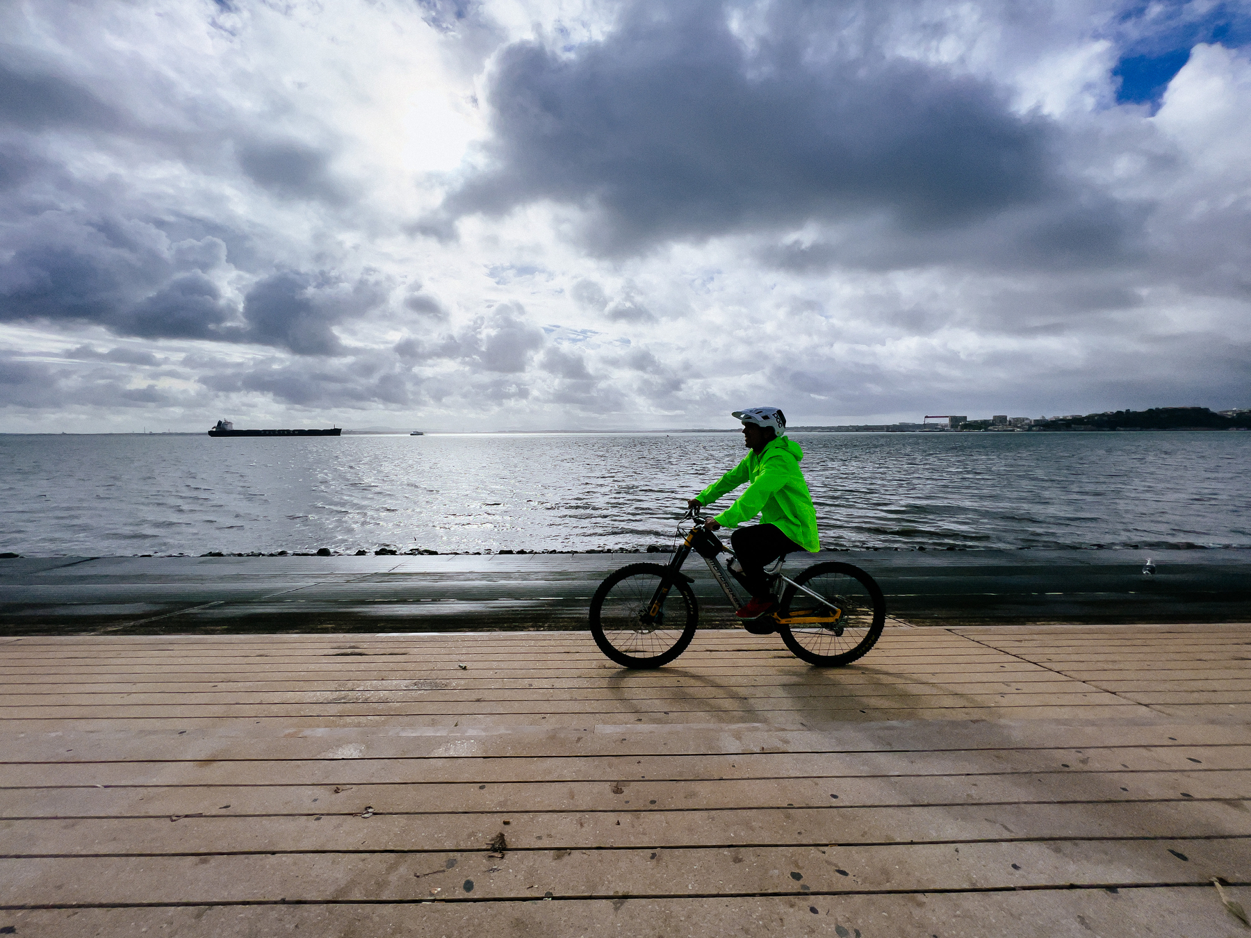 A cyclist rides along the river, on a cloudy day
