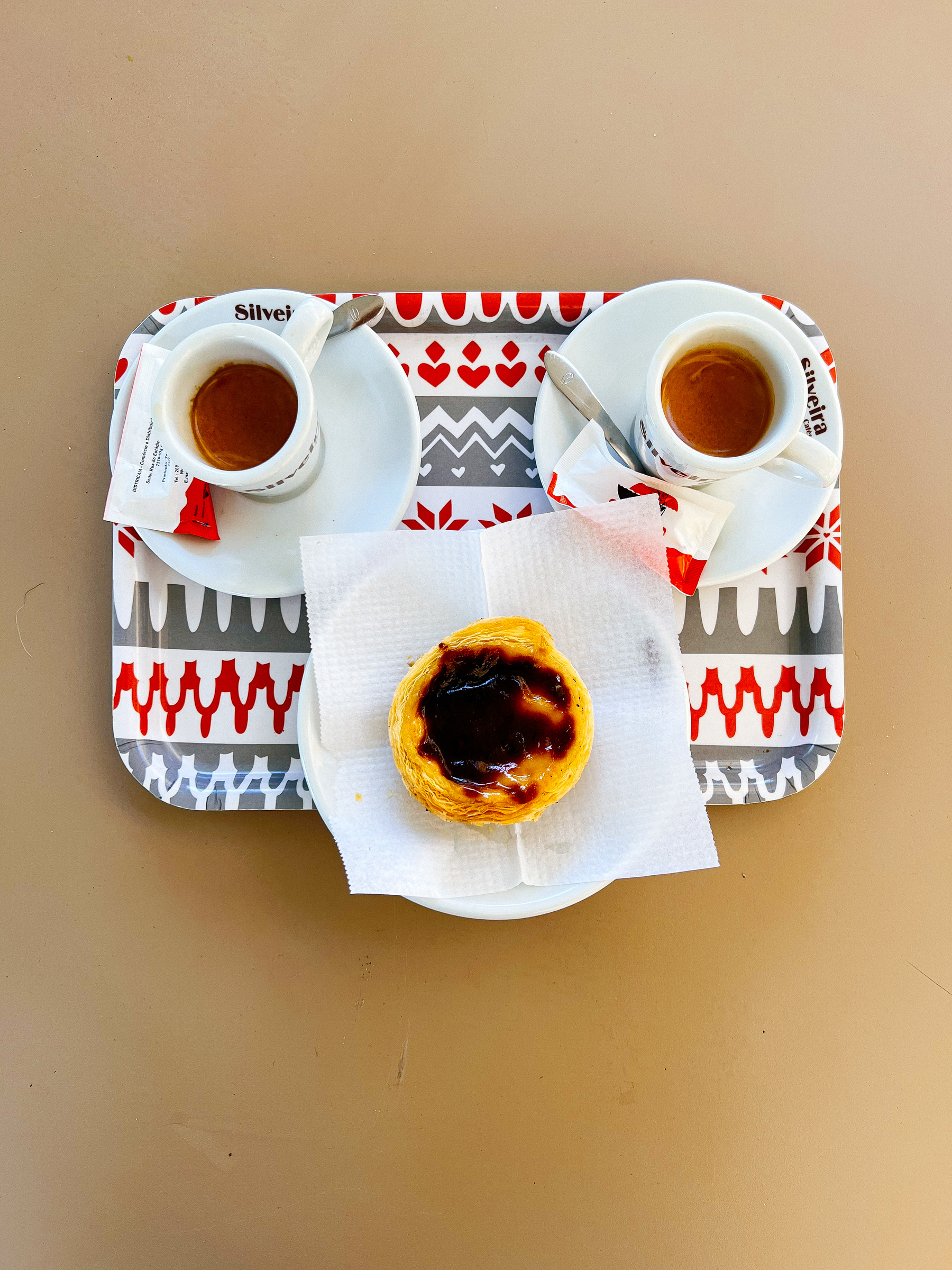 Looking down on a tray, two espressos and a pastel de nata look like a face. 