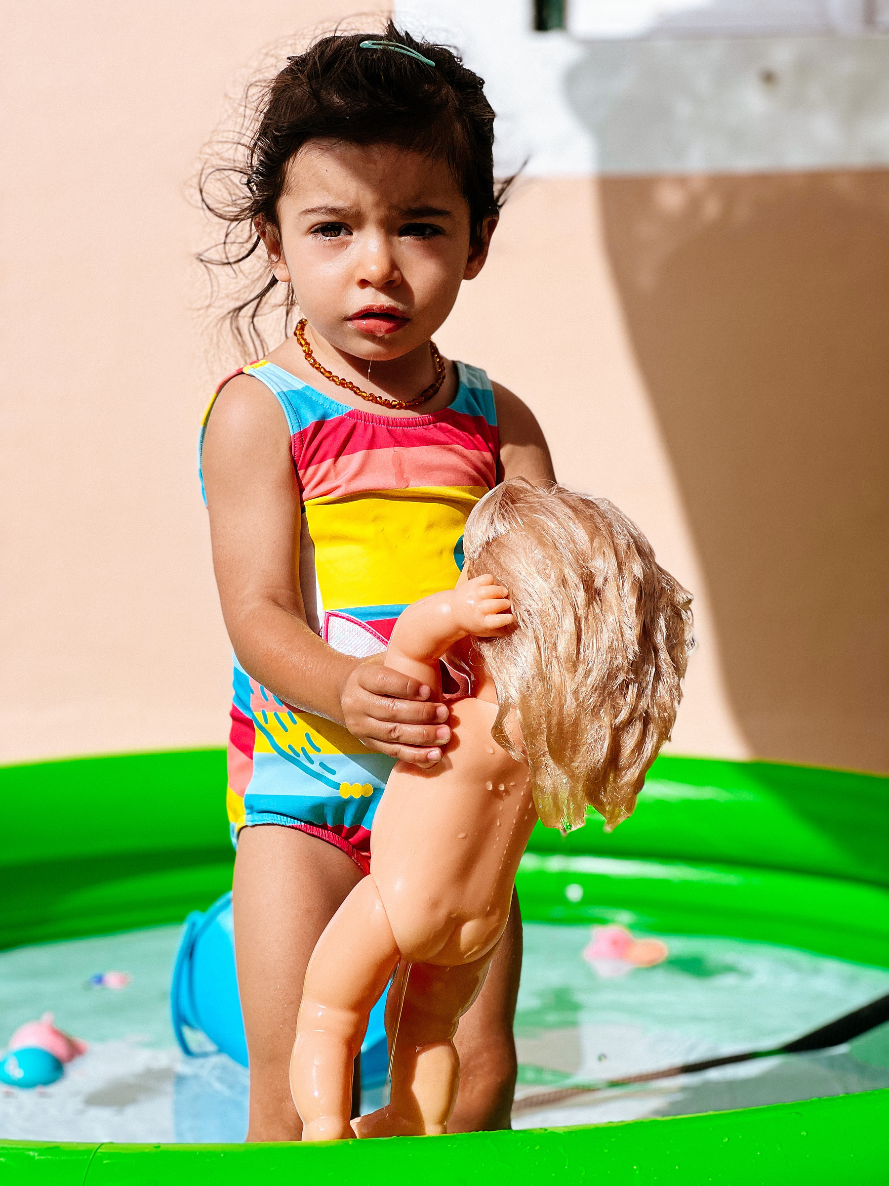Toddler in an inflatable pool, with a doll. 