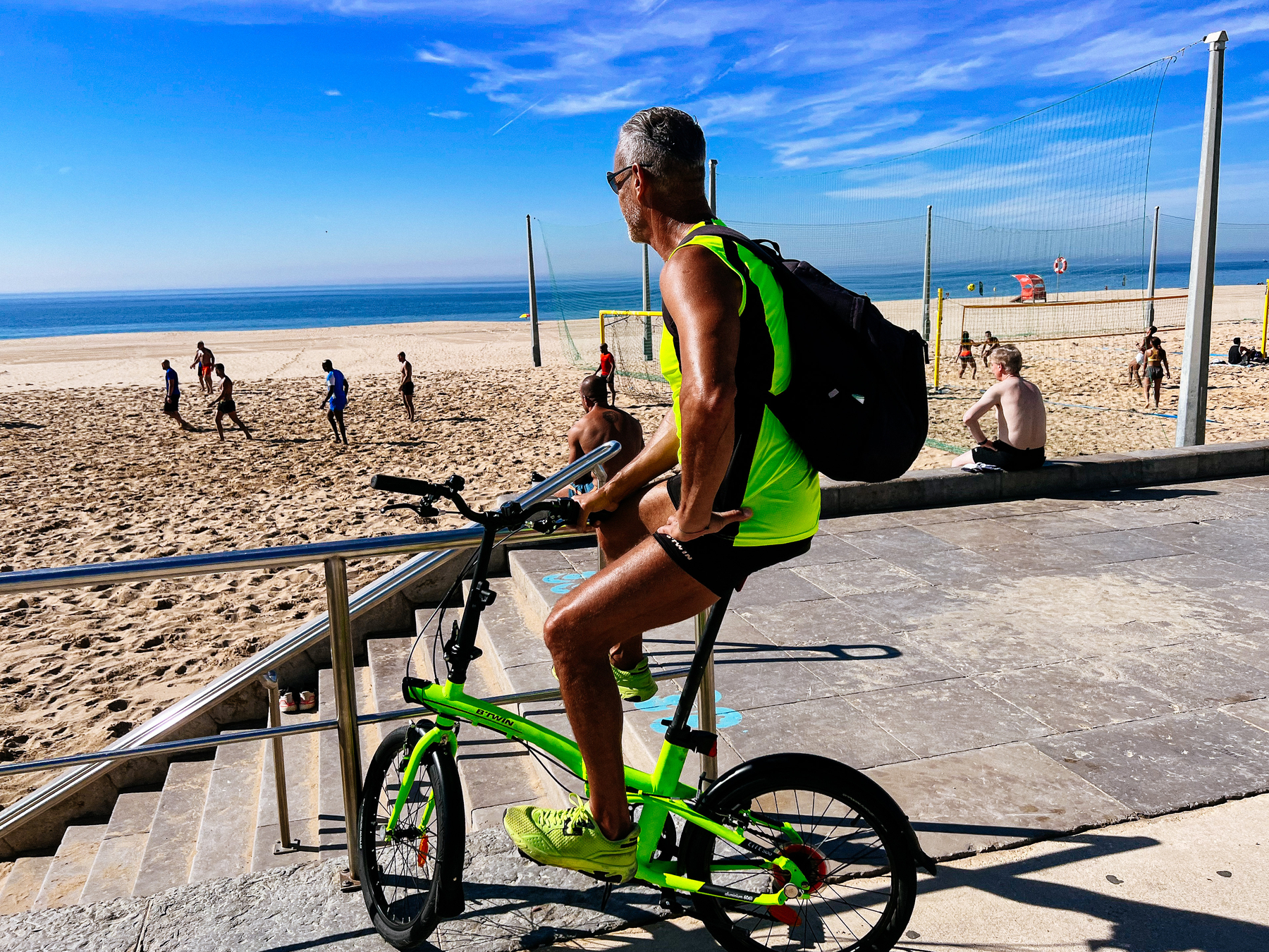 a cyclist looks at people playing at the beach