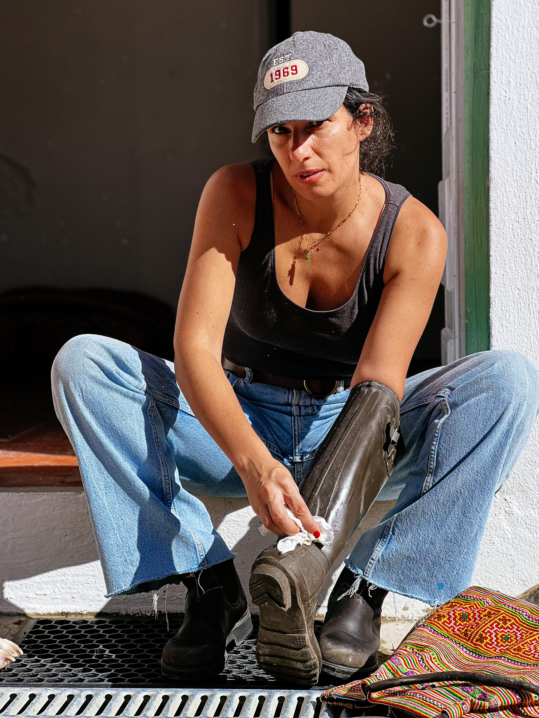 A woman cleans a boot, wearing a cap. Looking serious. 