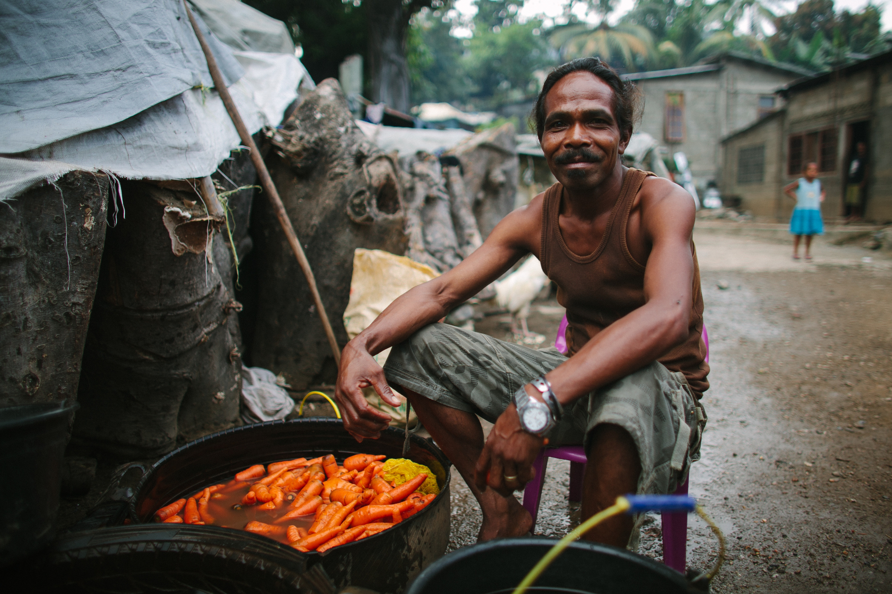 A man cooks a big pot of carrots in a poor neighborhood. 