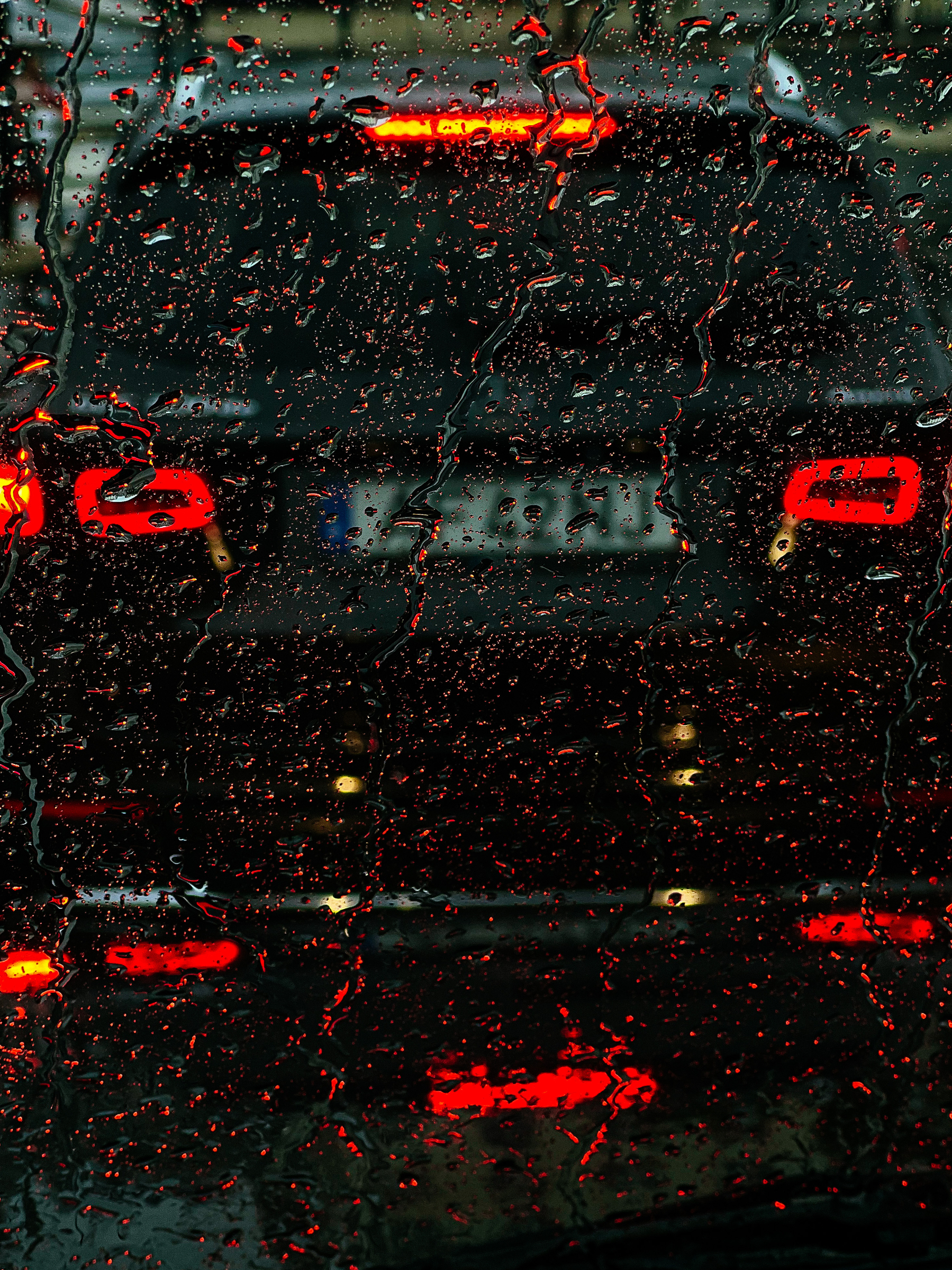 raindrops on a windshield, with red light coming from the stopped car just in front of us