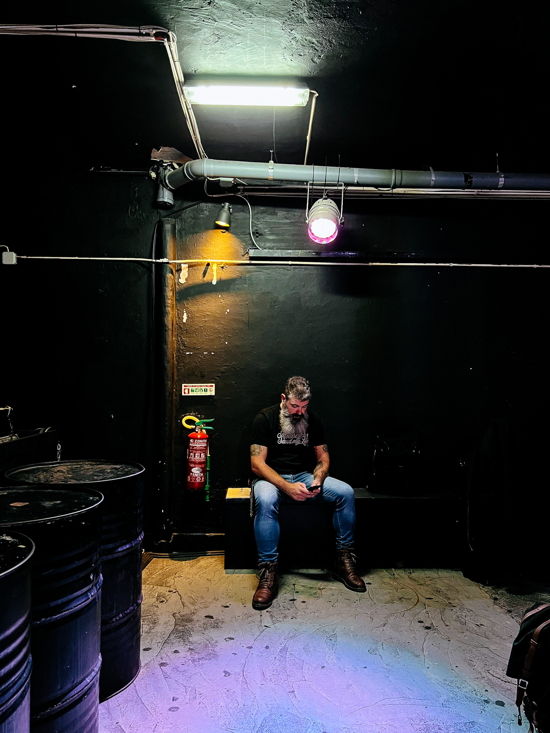 A man sits, using his phone, in a dark corner of a music club 