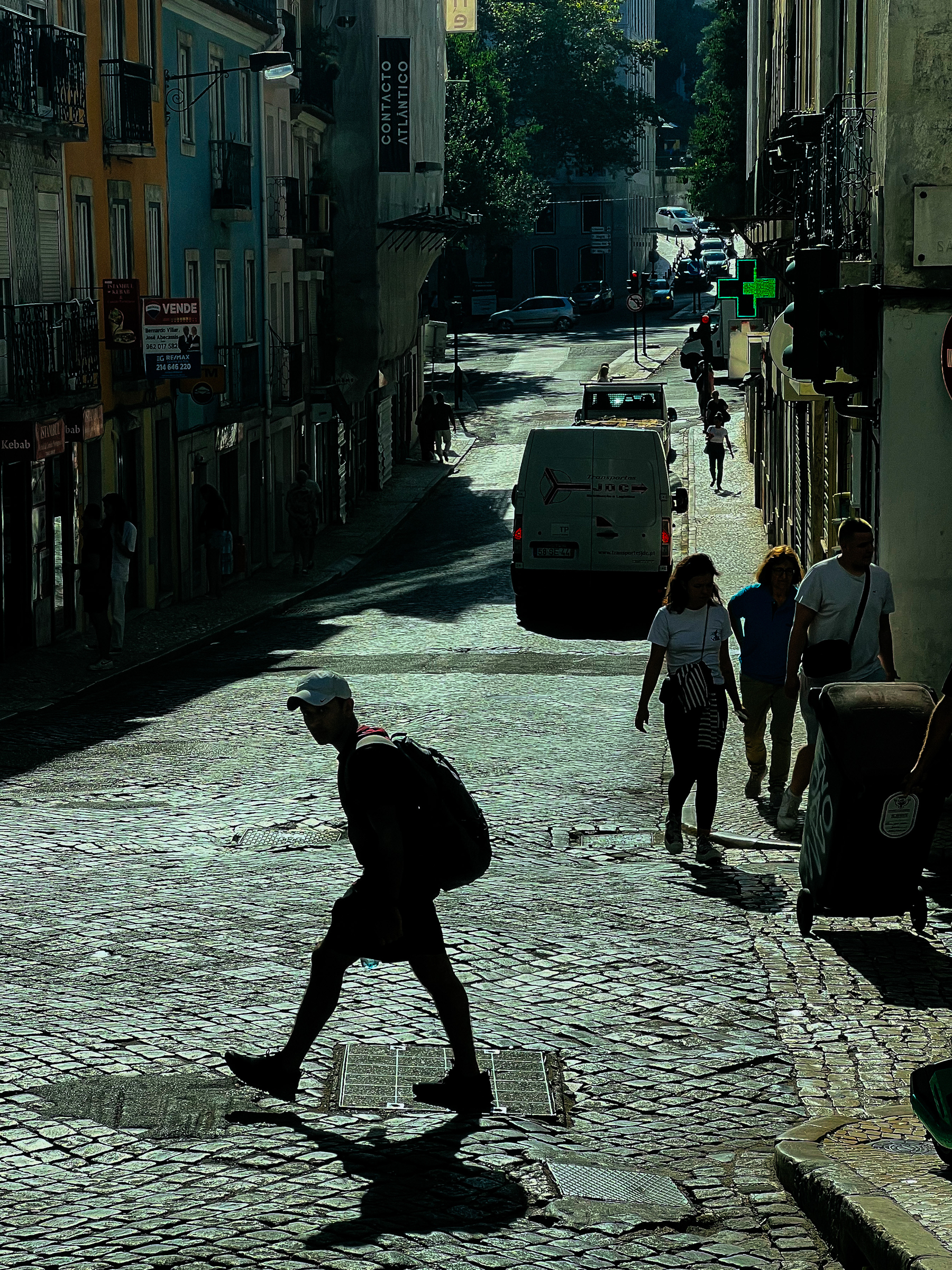 A man crosses a city street, dramatic backlight. Old part of town. 
