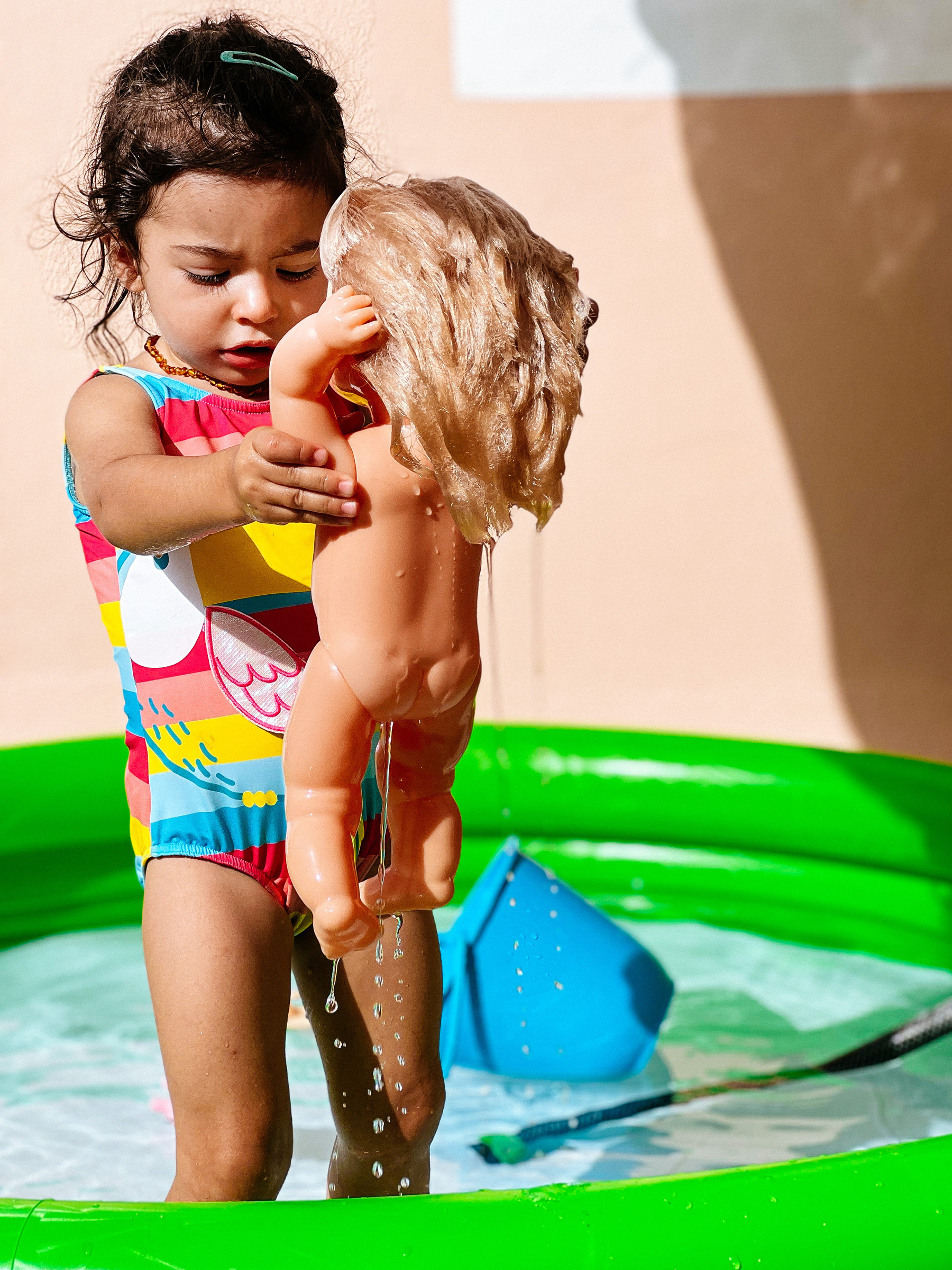 Toddler in an inflatable pool, with a doll. 