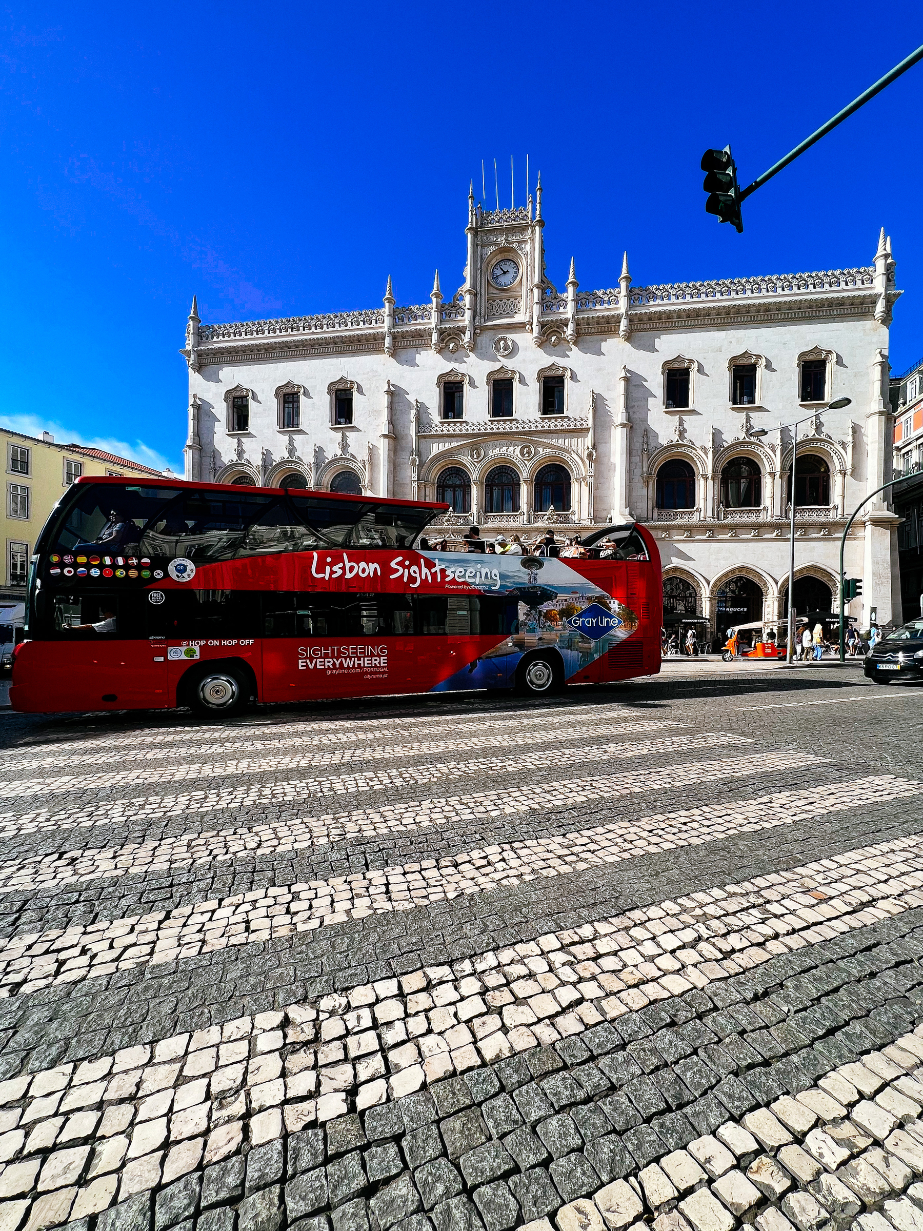A red bus with “Lisbon sightseeing” written on it, in front of a cool, old, building. 