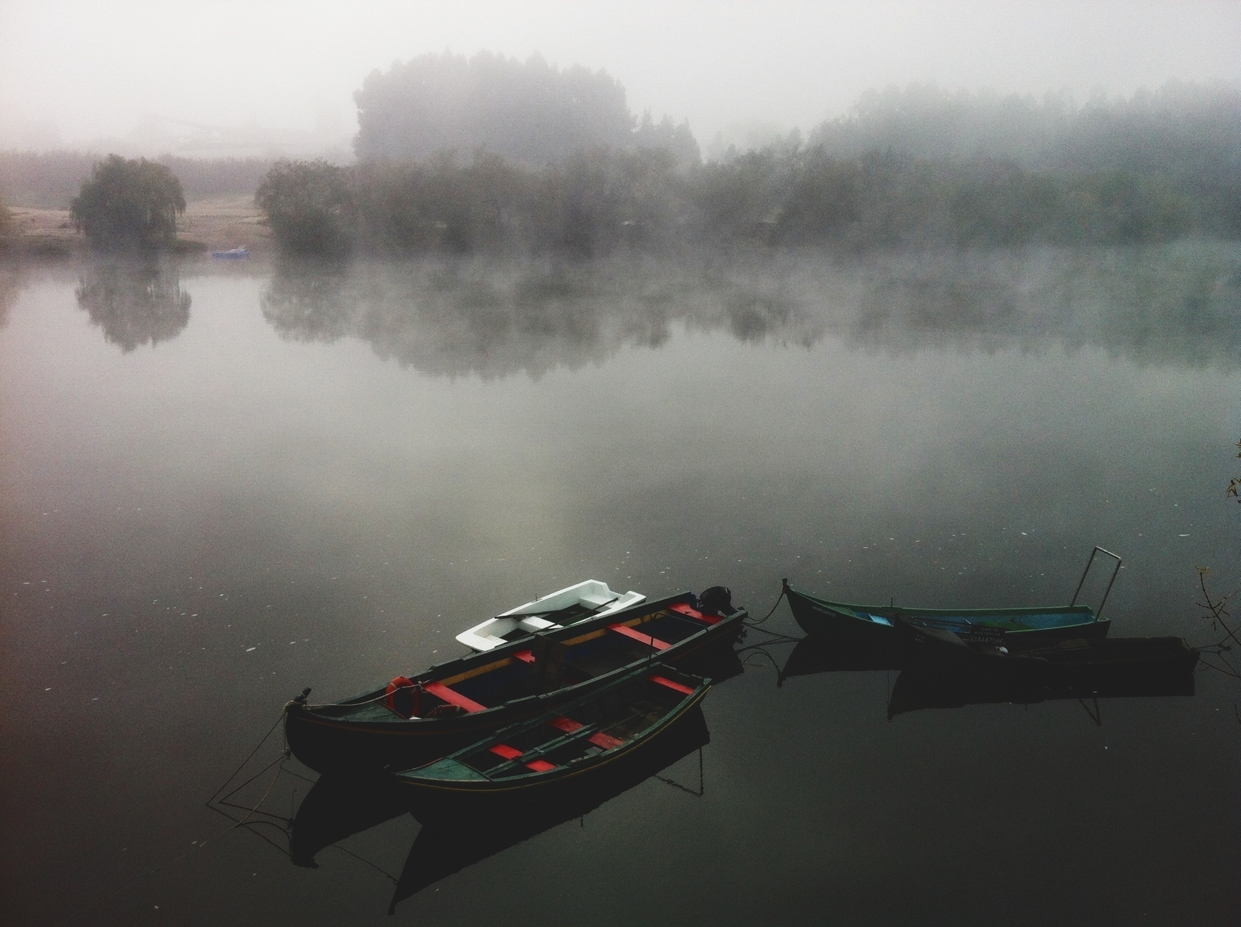 Boats rest on a very still river, with fog on the background.