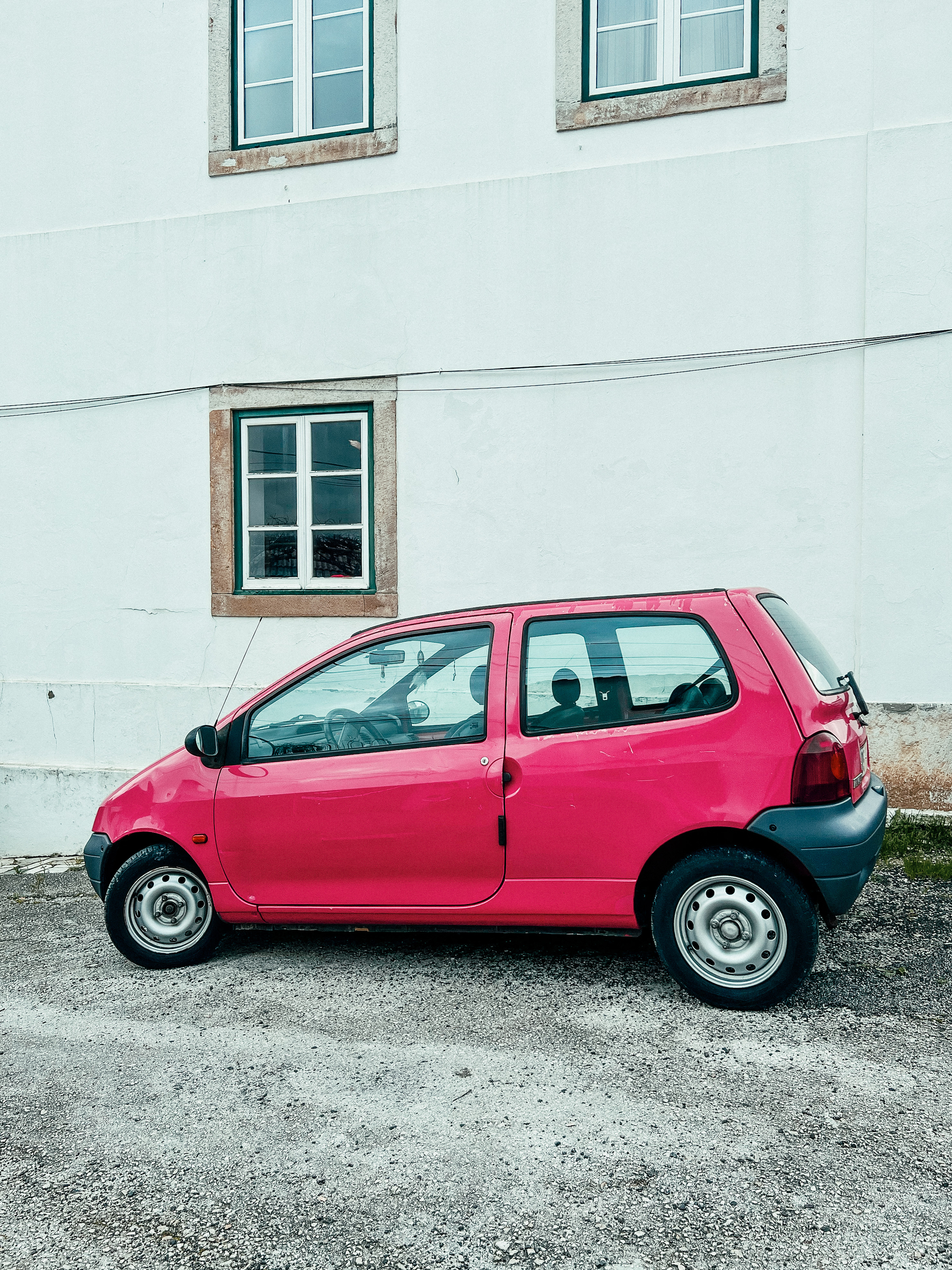 A pink car parked against a white wall. 