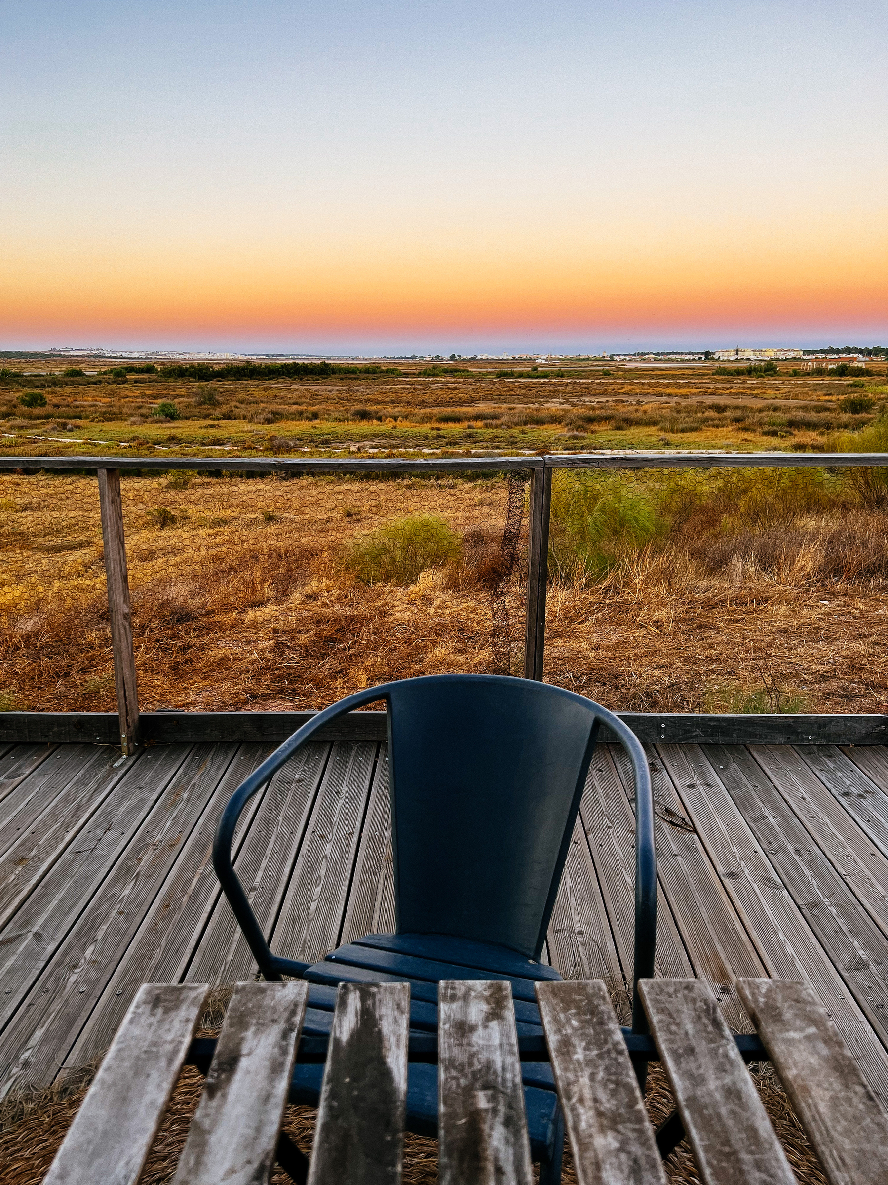 a chair and a table, during sunset. Empty landscape in the background.