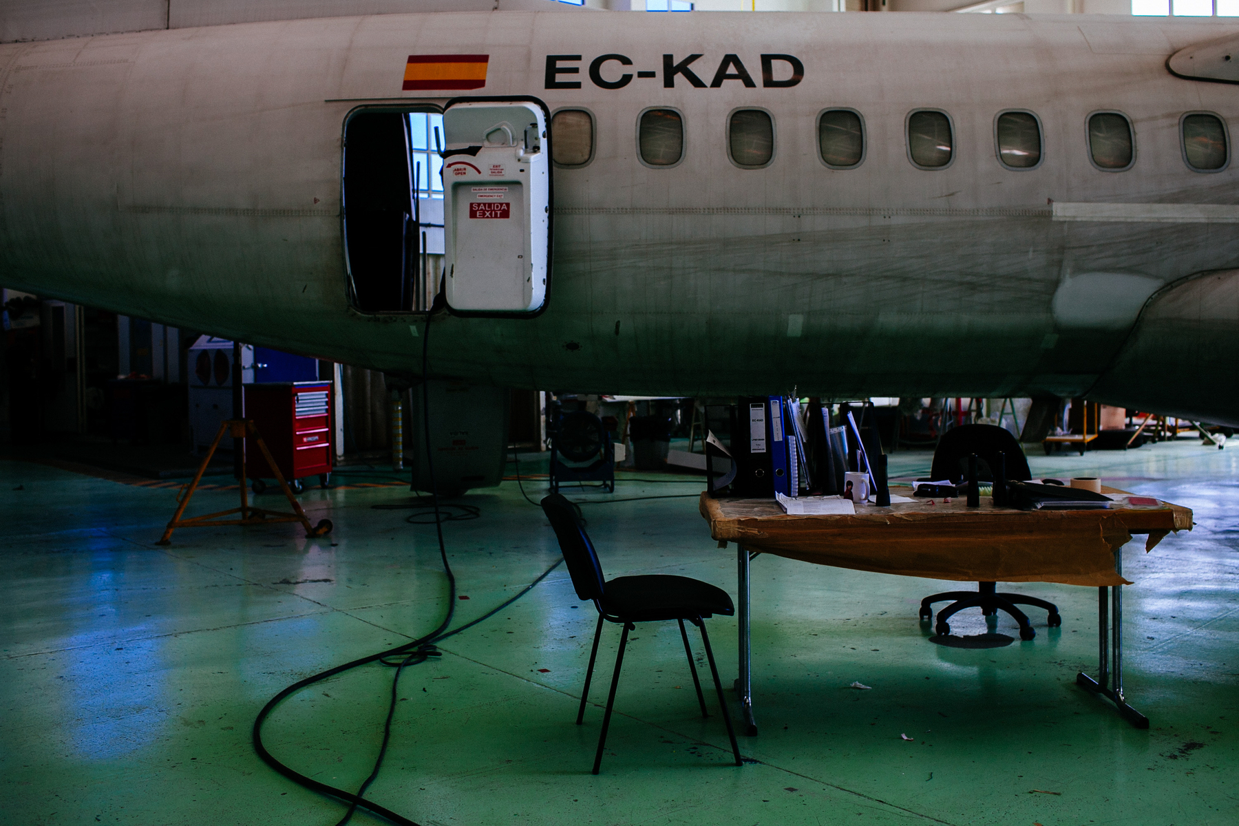 A chair in a hangar, with a plane behind it. 