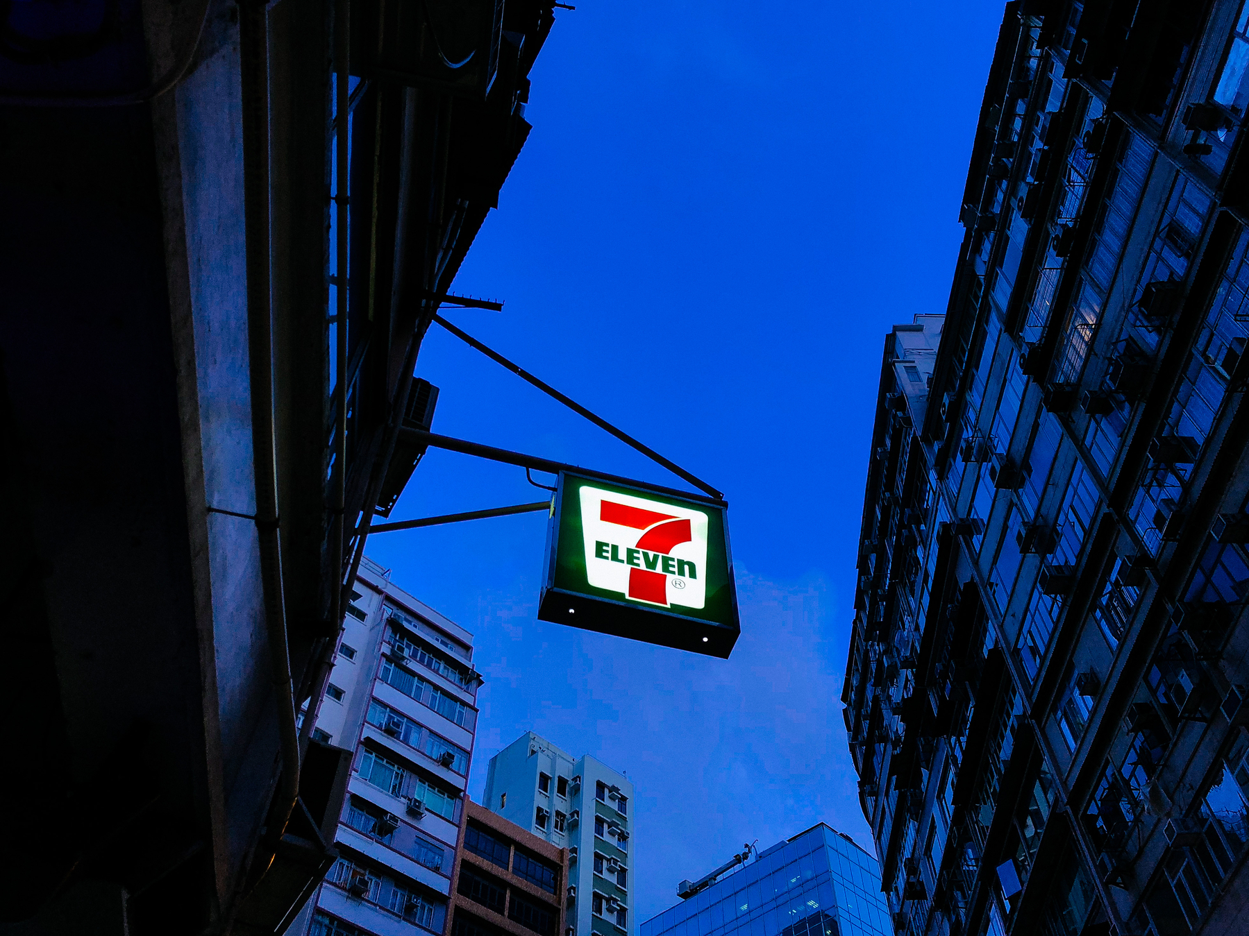 looking up to a 7-Eleven sign with a dusk sky above, in blue tones