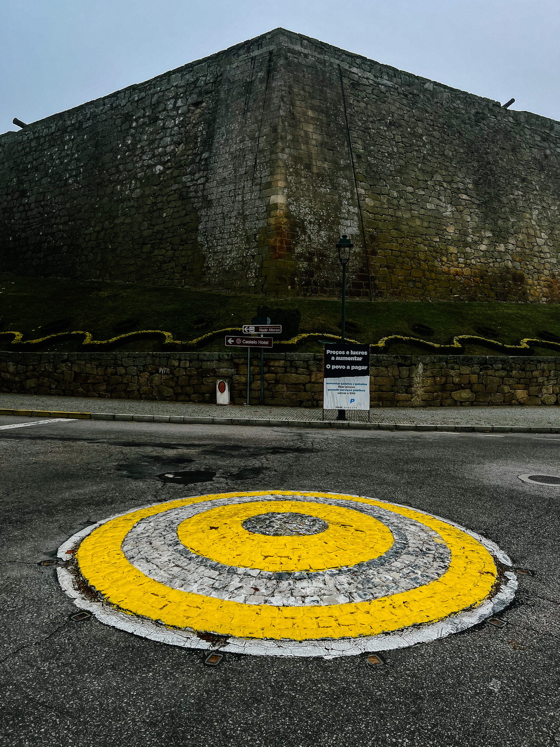 A very small roundabout painted yellow, with a dark fort wall behind it. 