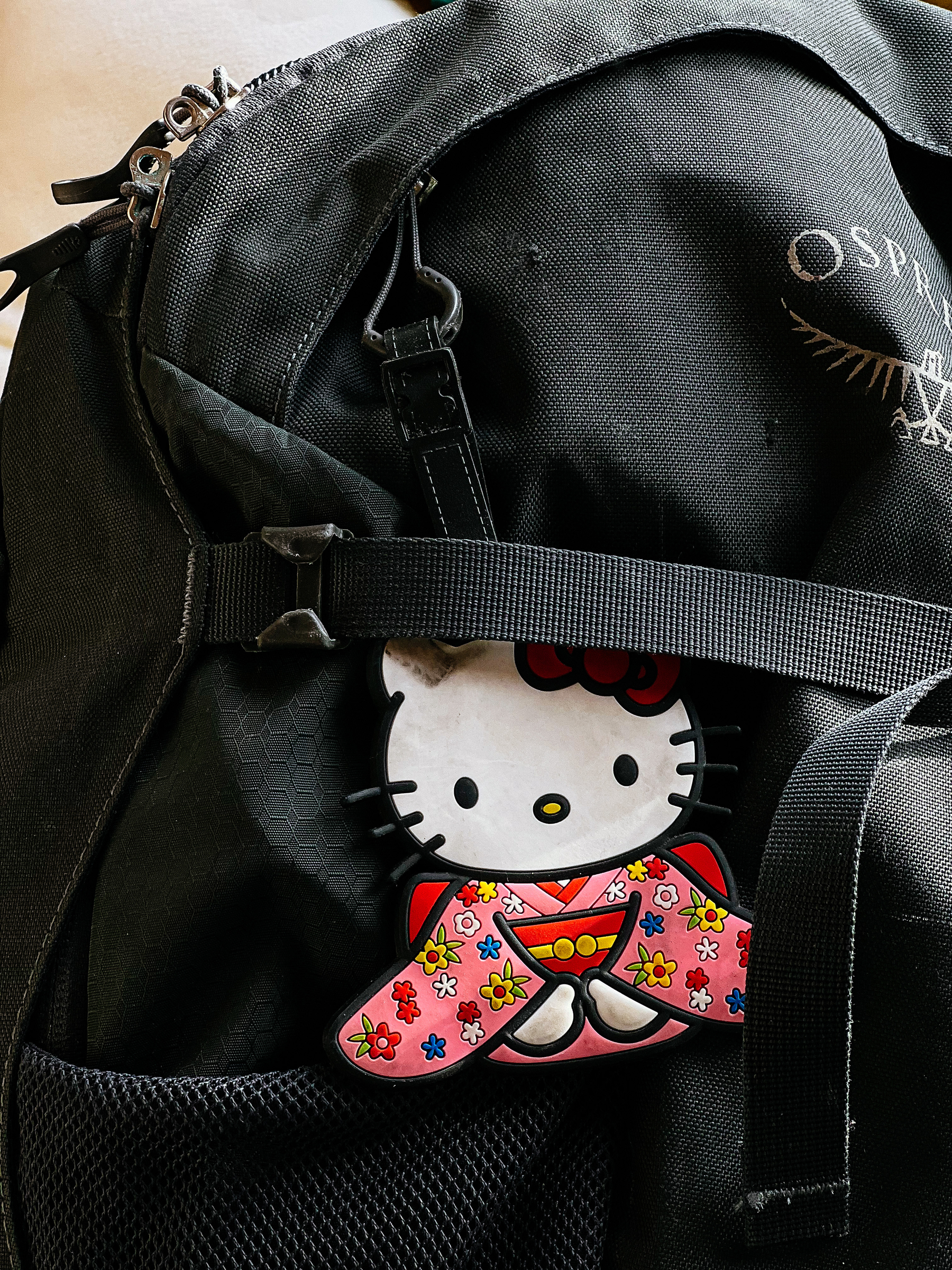 An Hello Kitty wearing a kimono luggage tag, strapped to a black backpack. 
