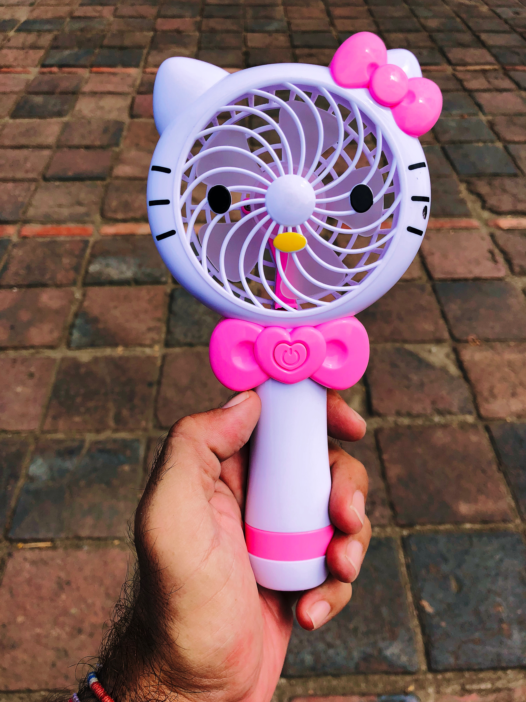 A hand holds a mini fan that looks like Hello Kitty