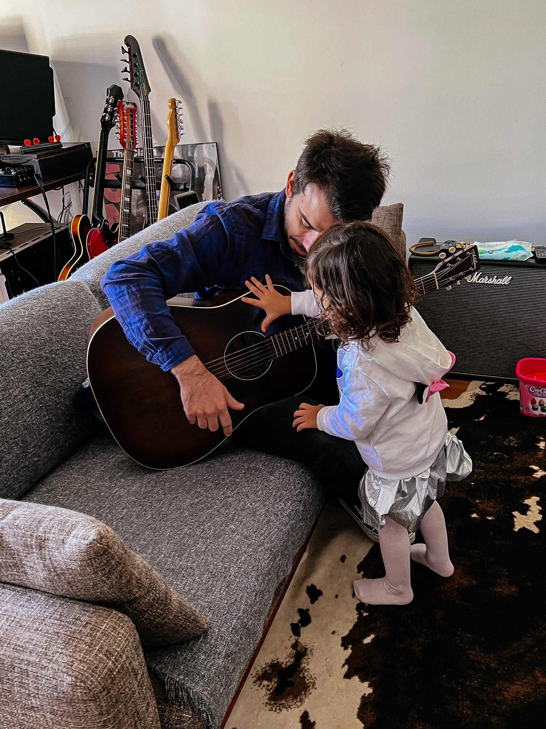 A man plays the guitar while a toddler touches the strings 
