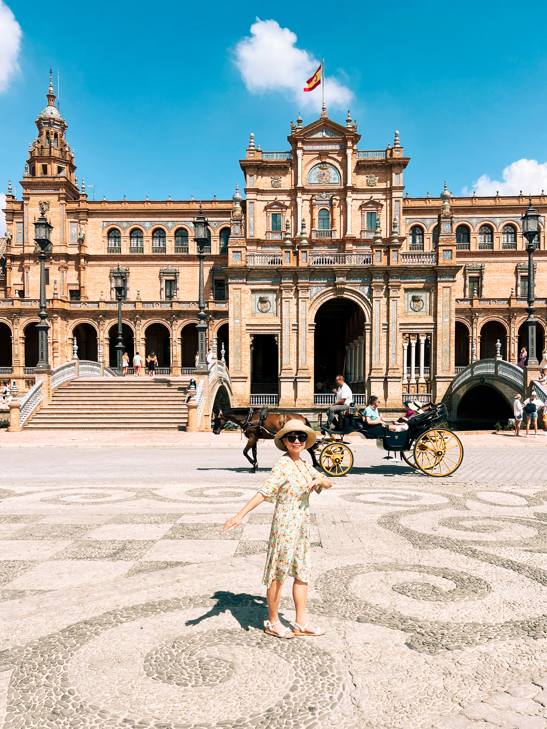 A tourist poses for a photo at Plaza de España, while a carriage goes by in the background. 