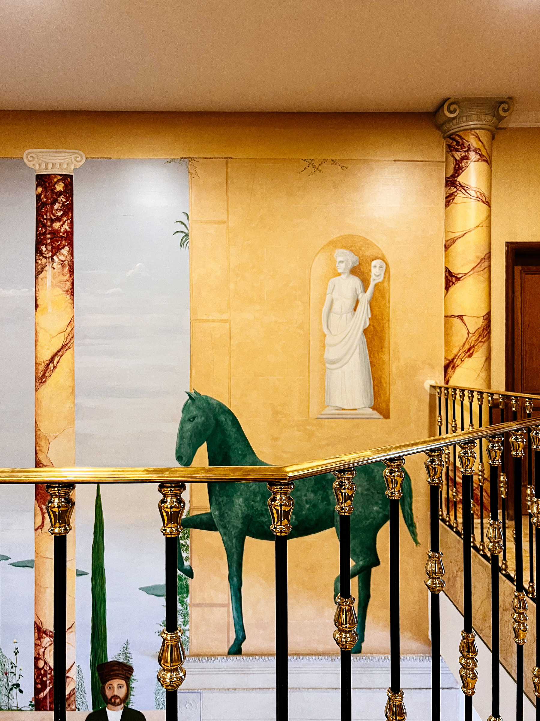 Part of a hotel lobby, a “fresco” is painted on the wall. A horse, columns, and a statue. 