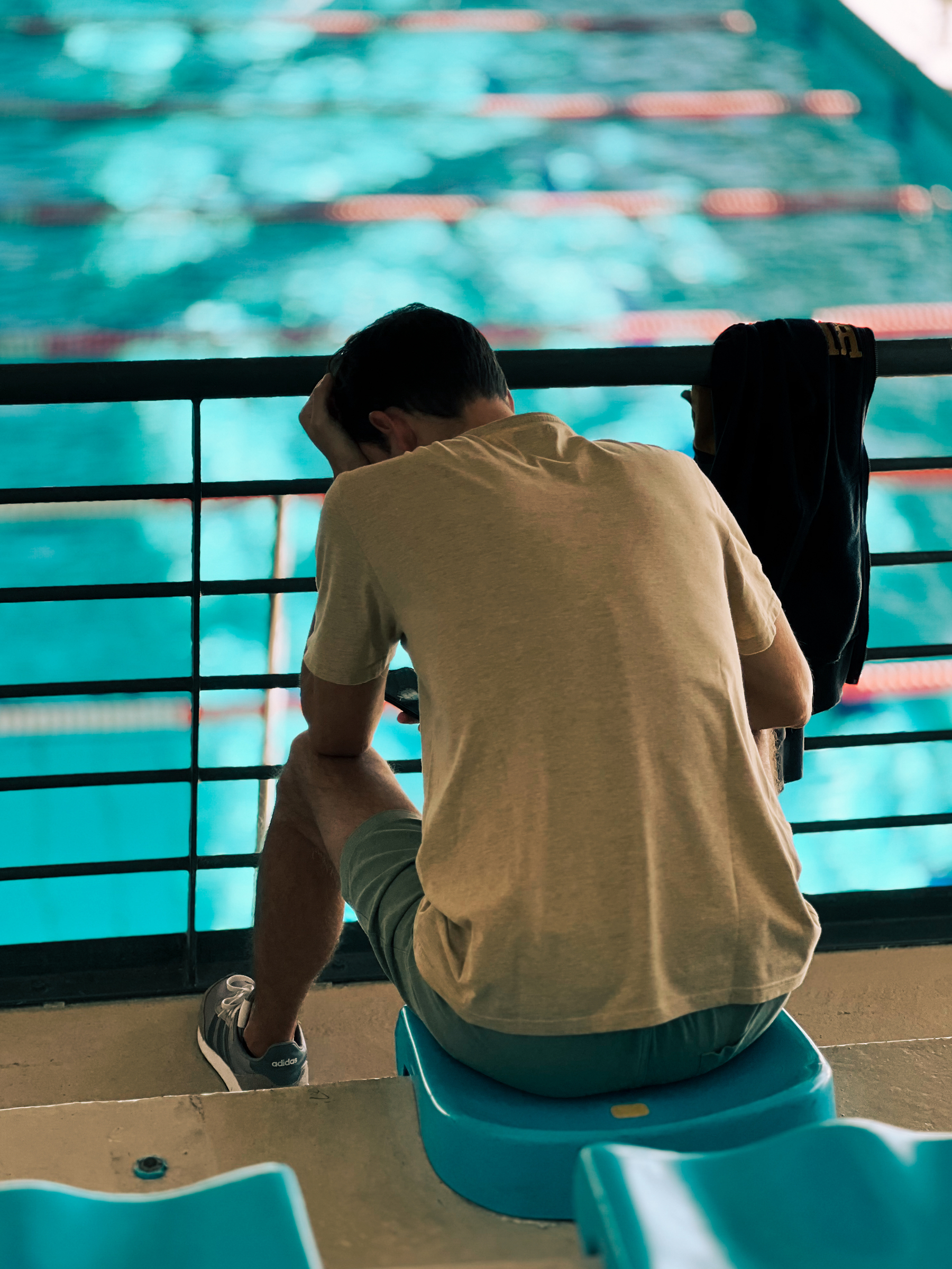A man looks at his phone, with a swimming pool in the background.