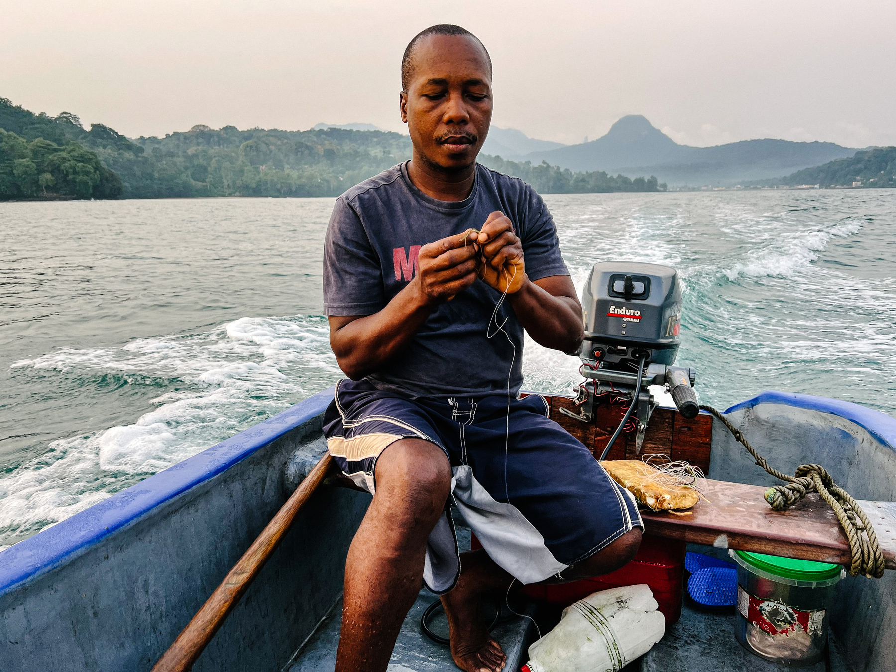 A fisherman preparing the line for a fishing day. He’s on his boat, land in the background. 