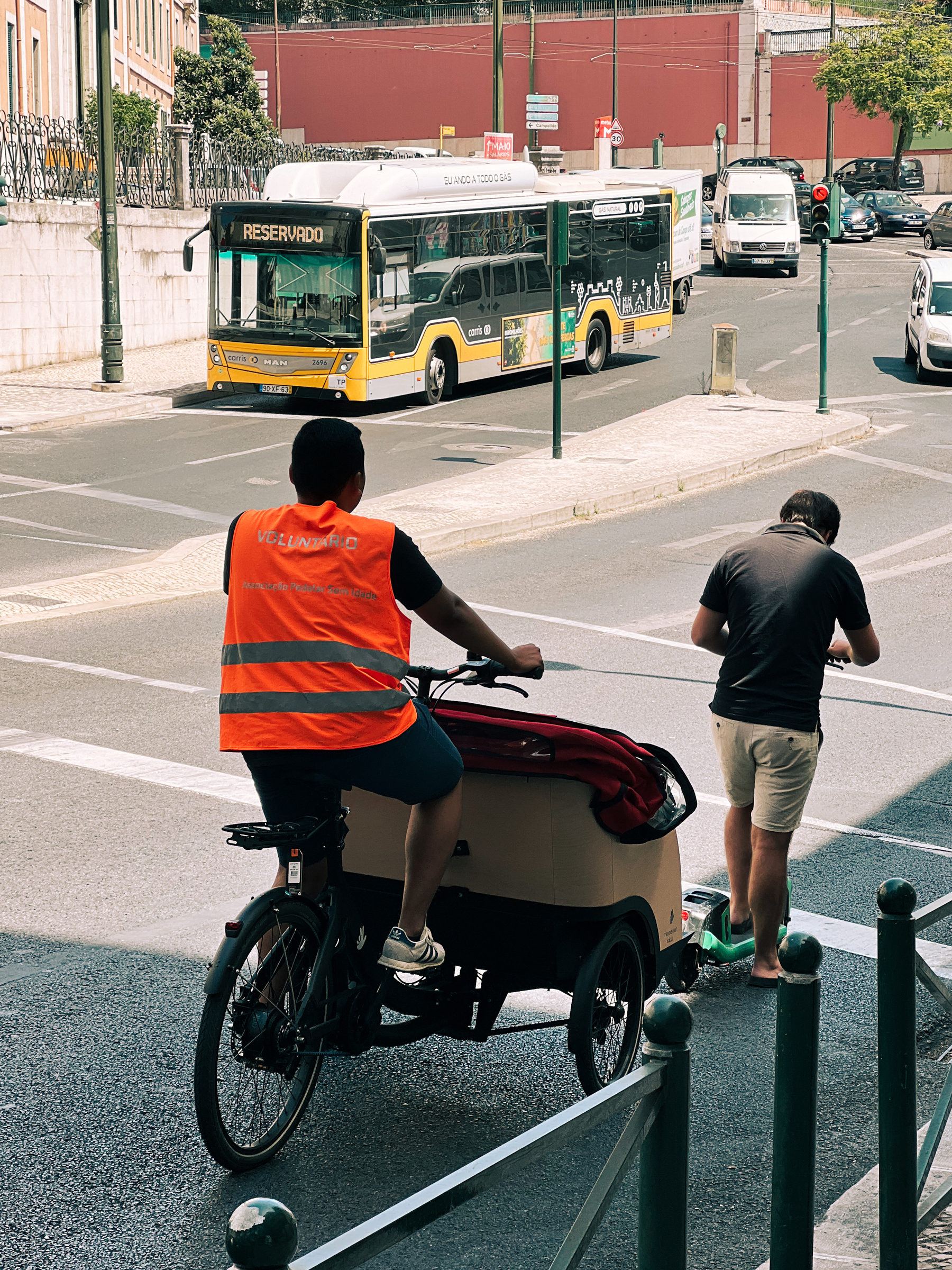 A tricycle rider, and a scooter rider, are the only two vehicles waiting for the light to turn green. 