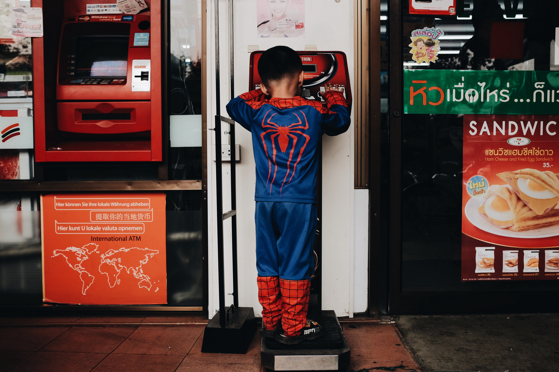 A boy dressed as Spiderman plays with an ATM.