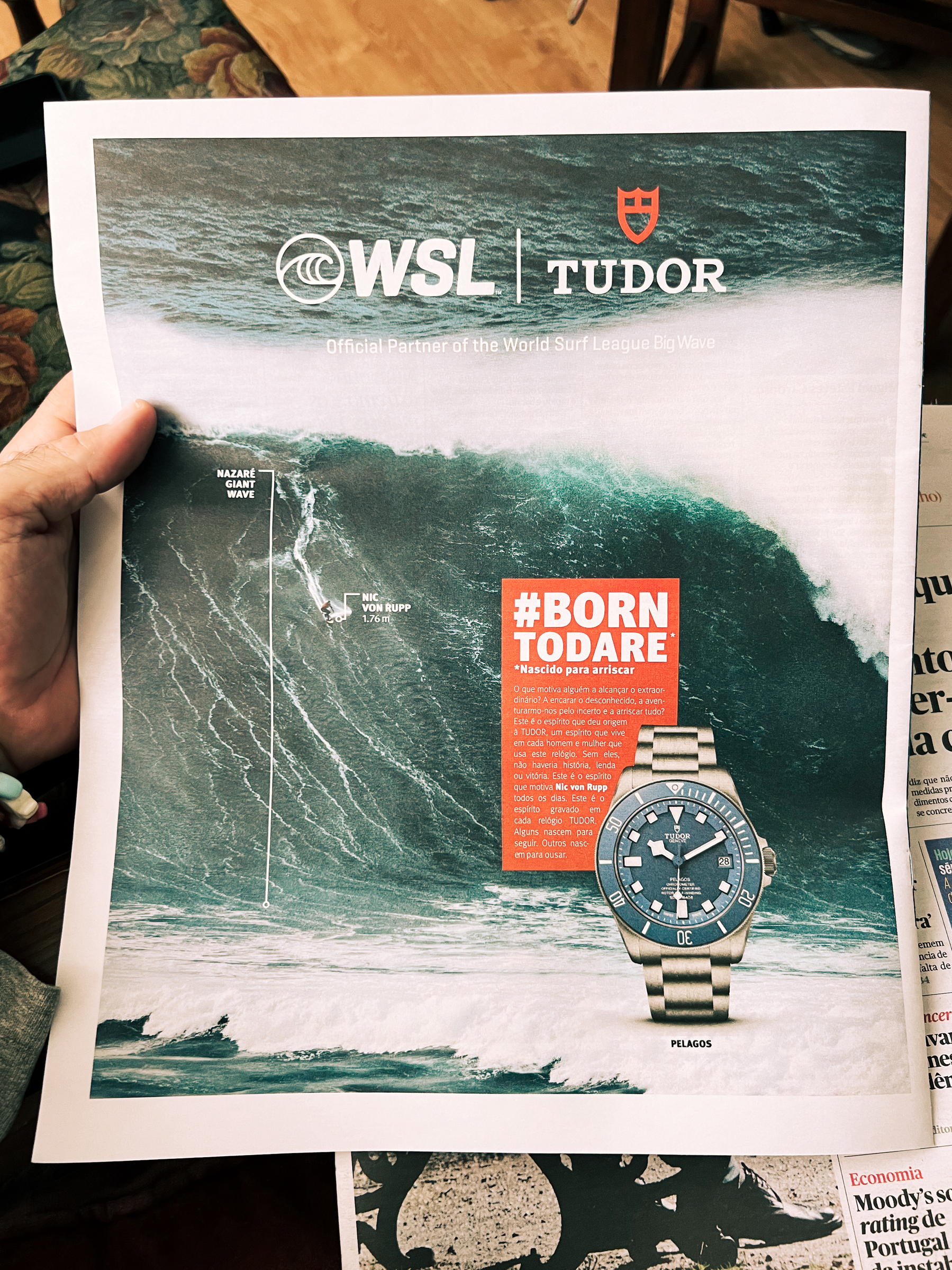 A watch ad, showing the giant wave of Nazaré, a surfer, and a Tudor watch.