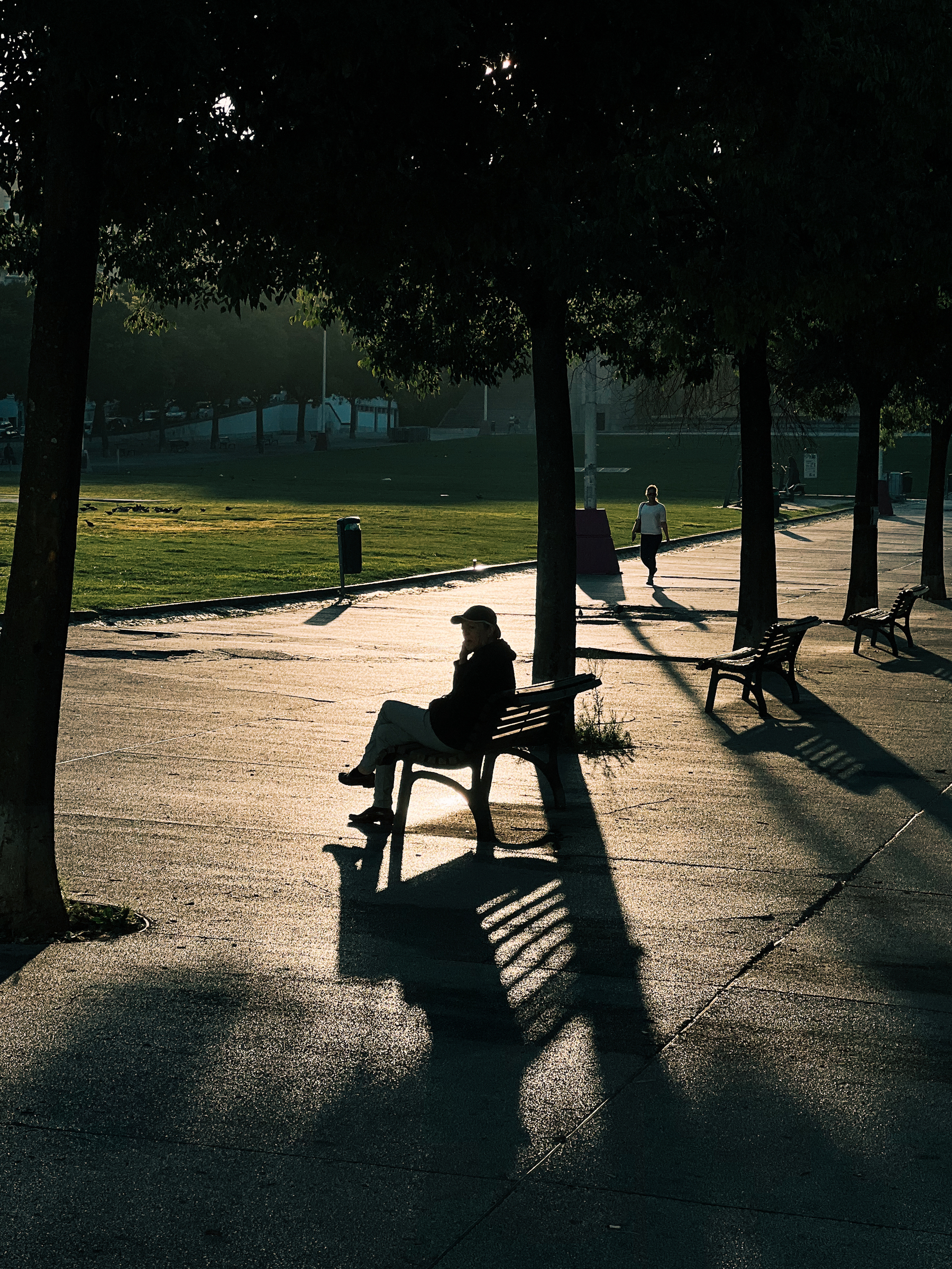 Smoker sits in a park bench, early morning sun. 