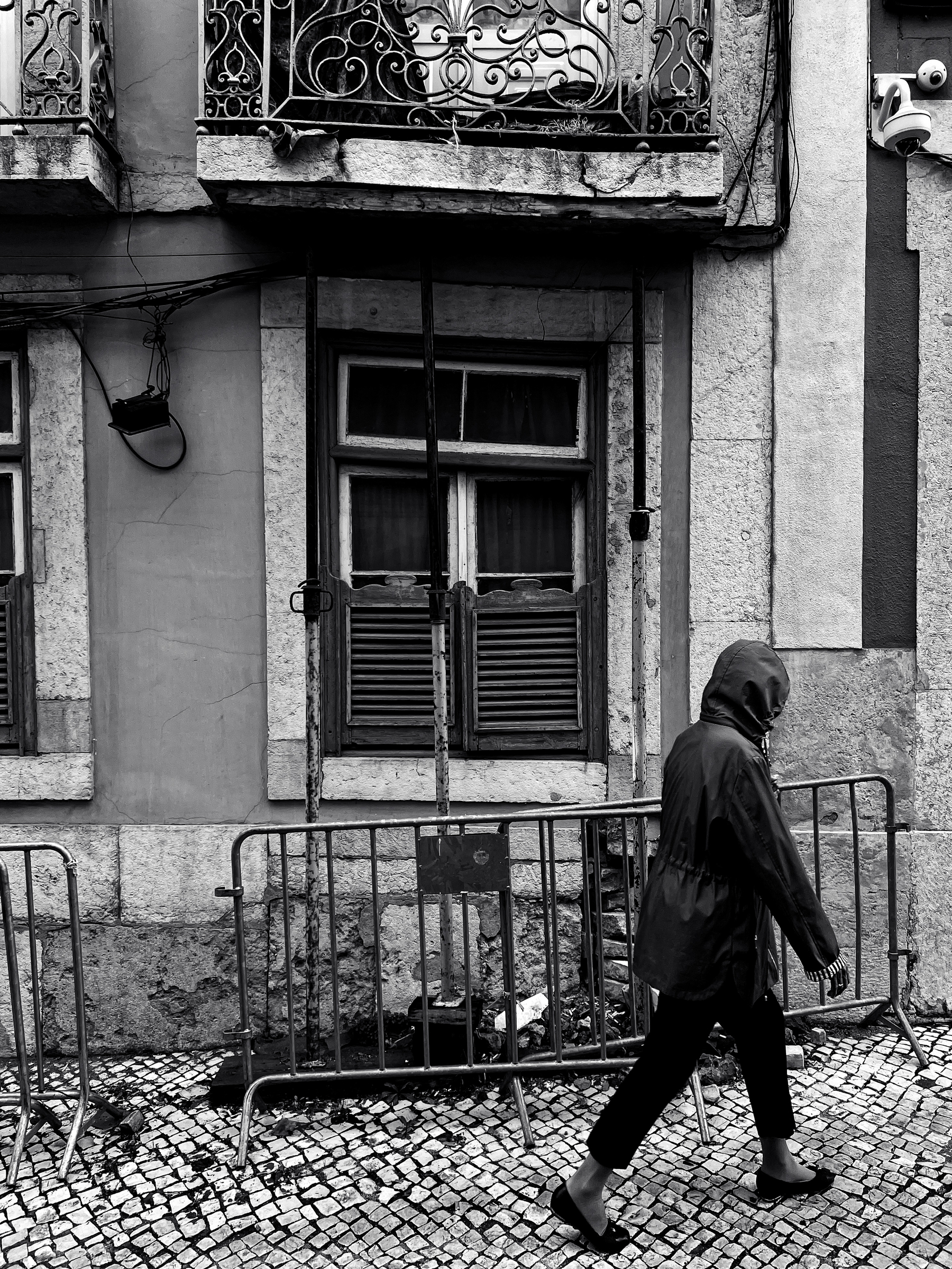 black and white photo of a person walking by a building that is derelict, almost collapsing.