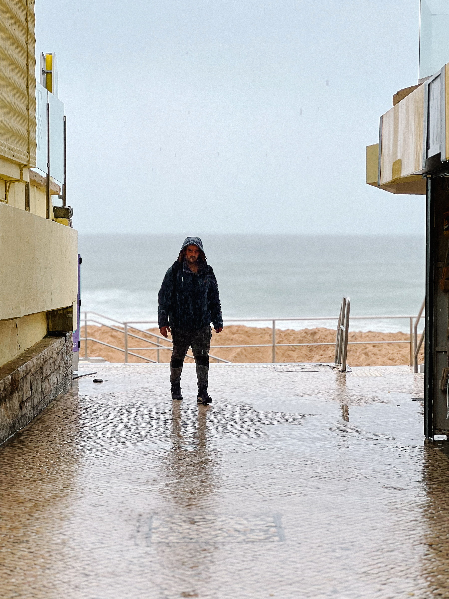 A man walks towards us, in rain gear. The ocean as a backdrop. 
