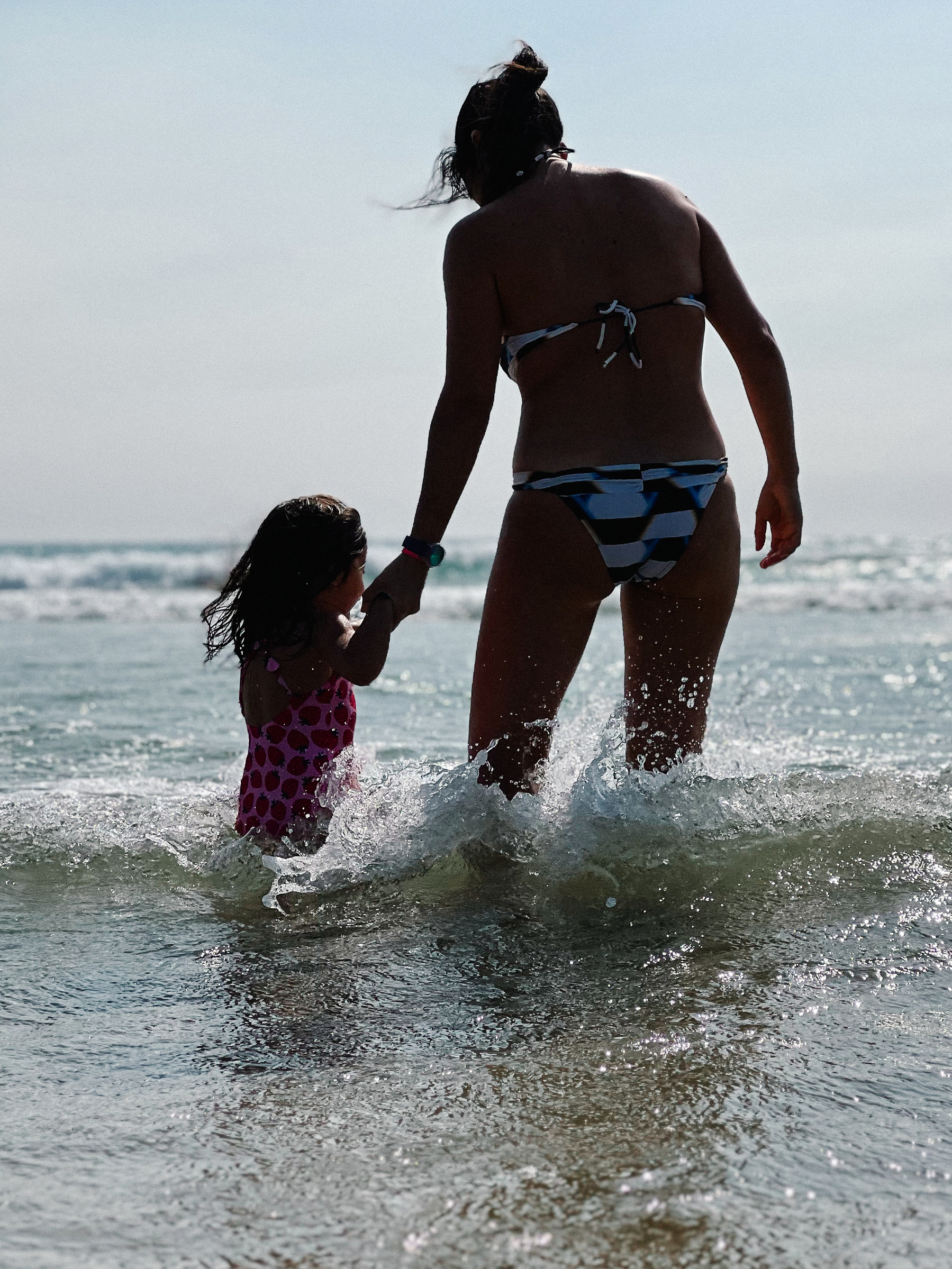 A girl and her mom, holding hands, in the sea. 