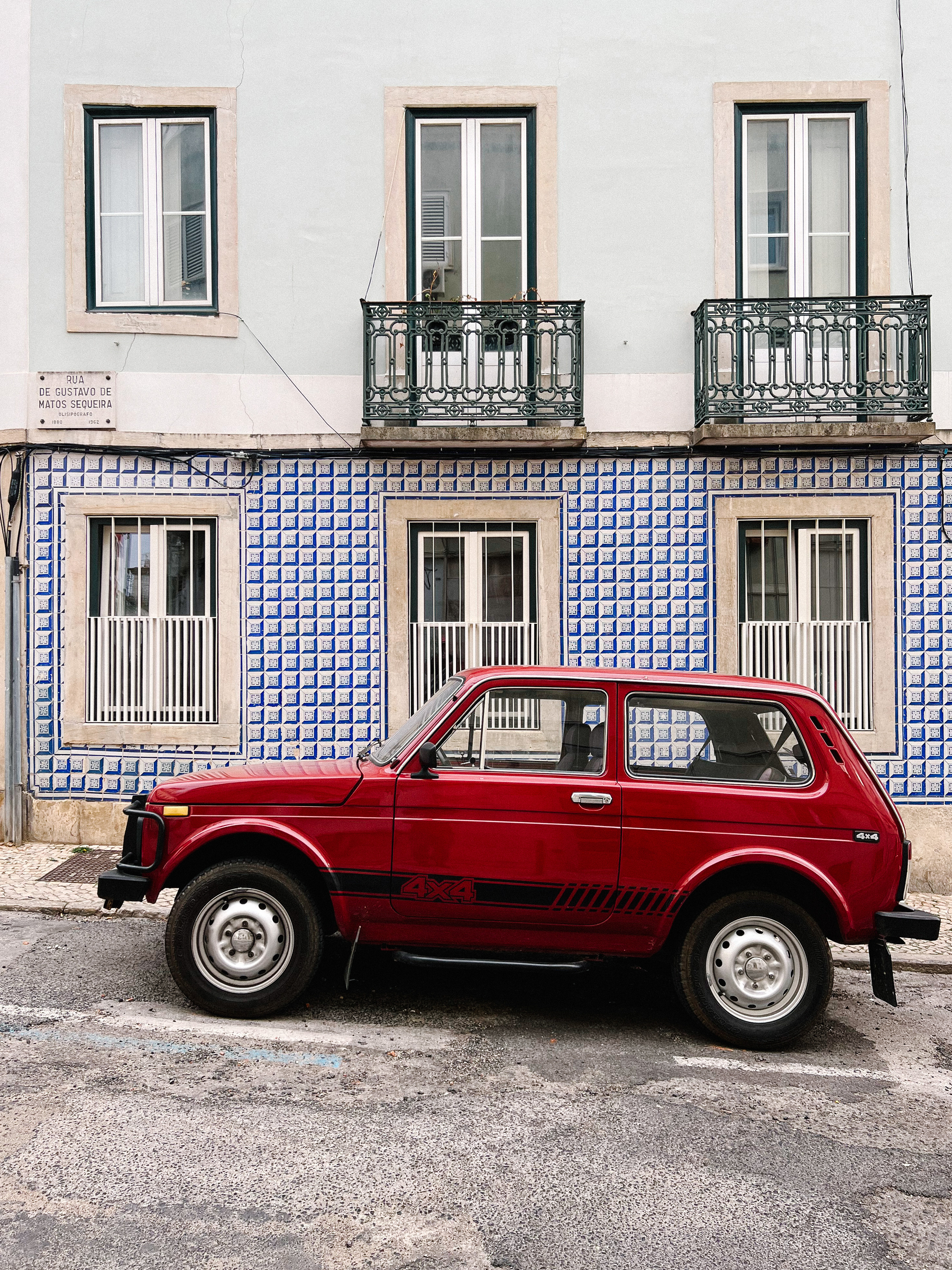 A red Lada Niva parked in front of a tile covered building. 