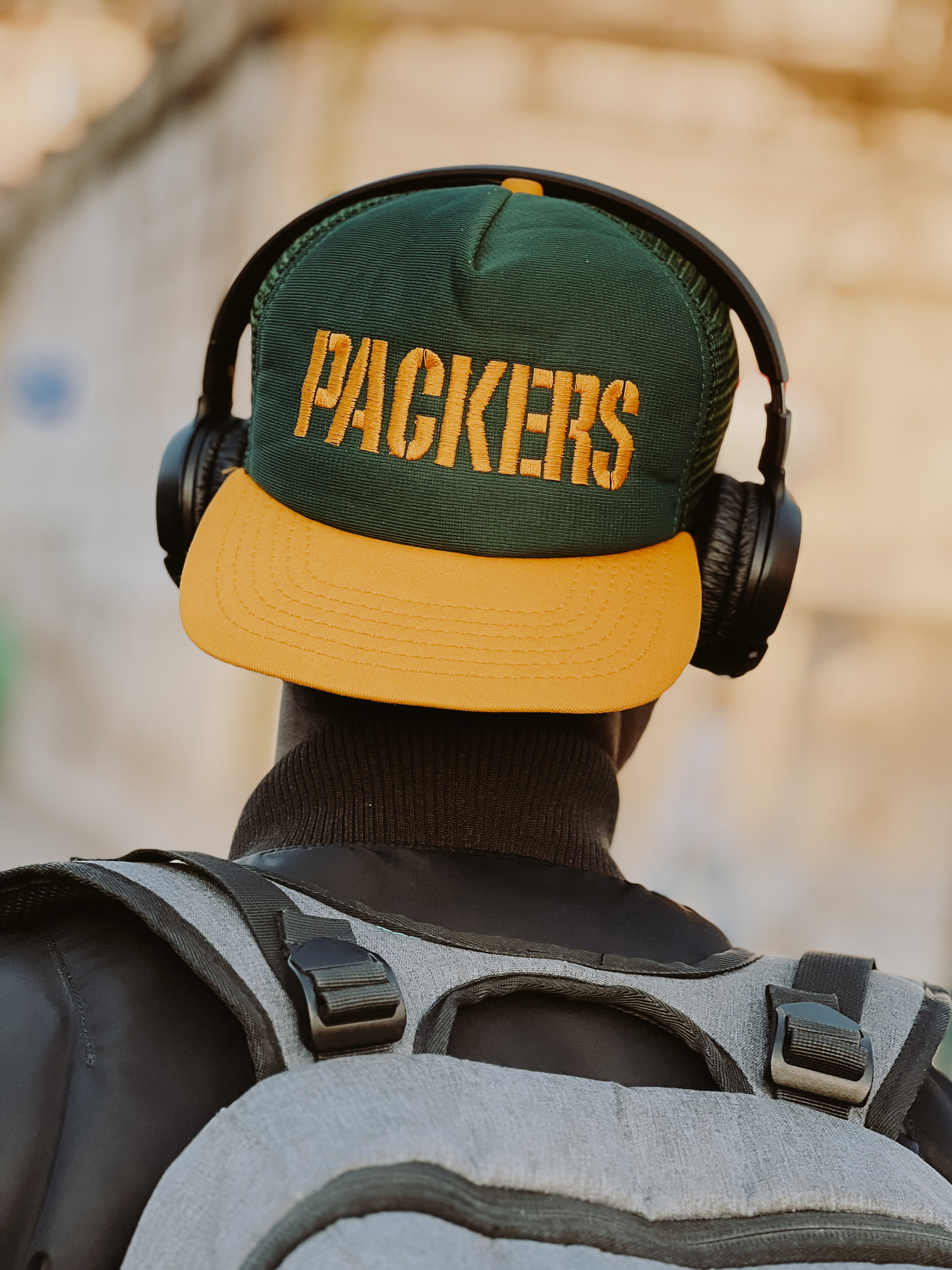A man wears a Packers hat, with headphones over it. His back turned to us. 